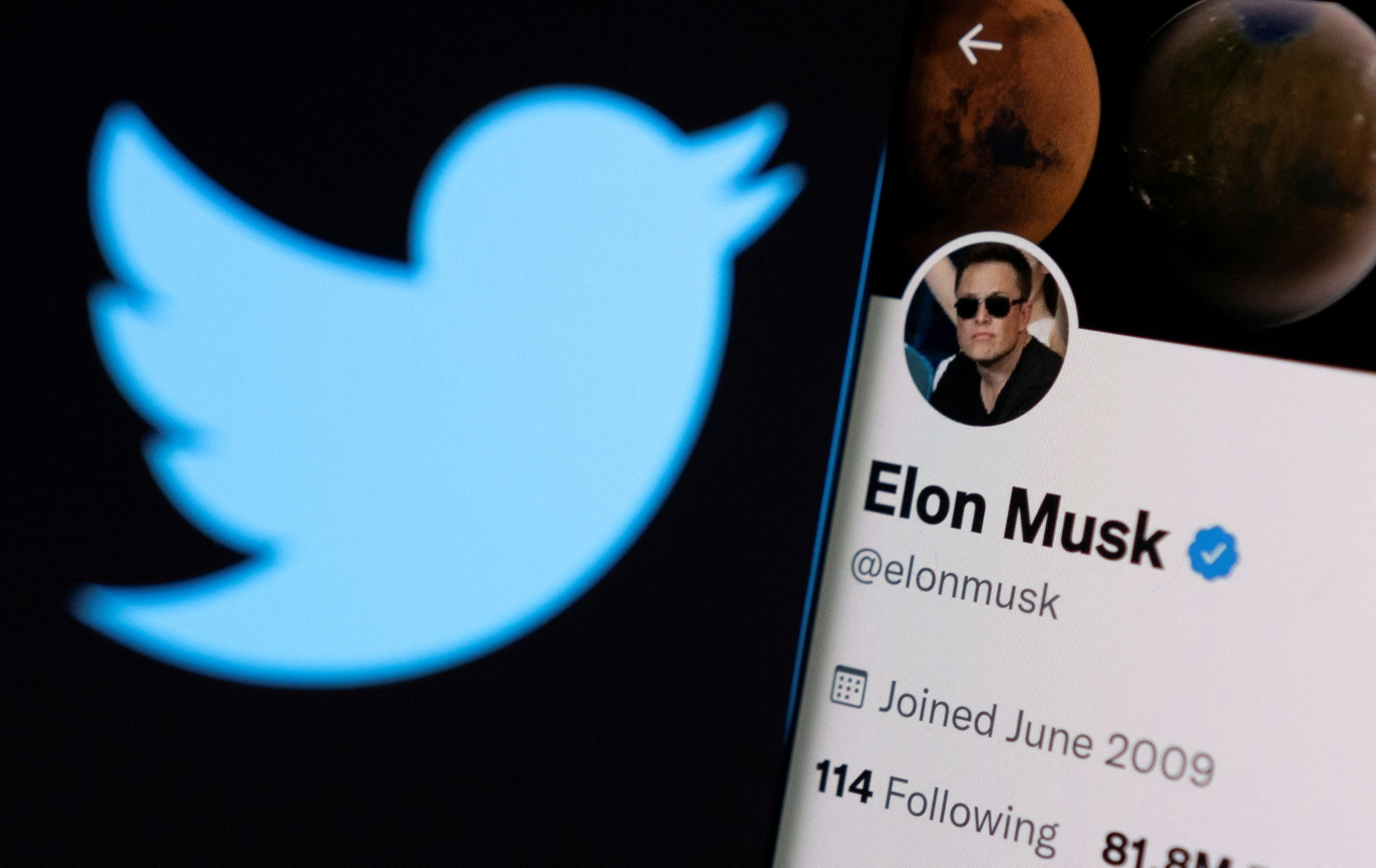 Elon Musk's twitter account is seen on a smartphone in front of the Twitter logo in this photo illustration