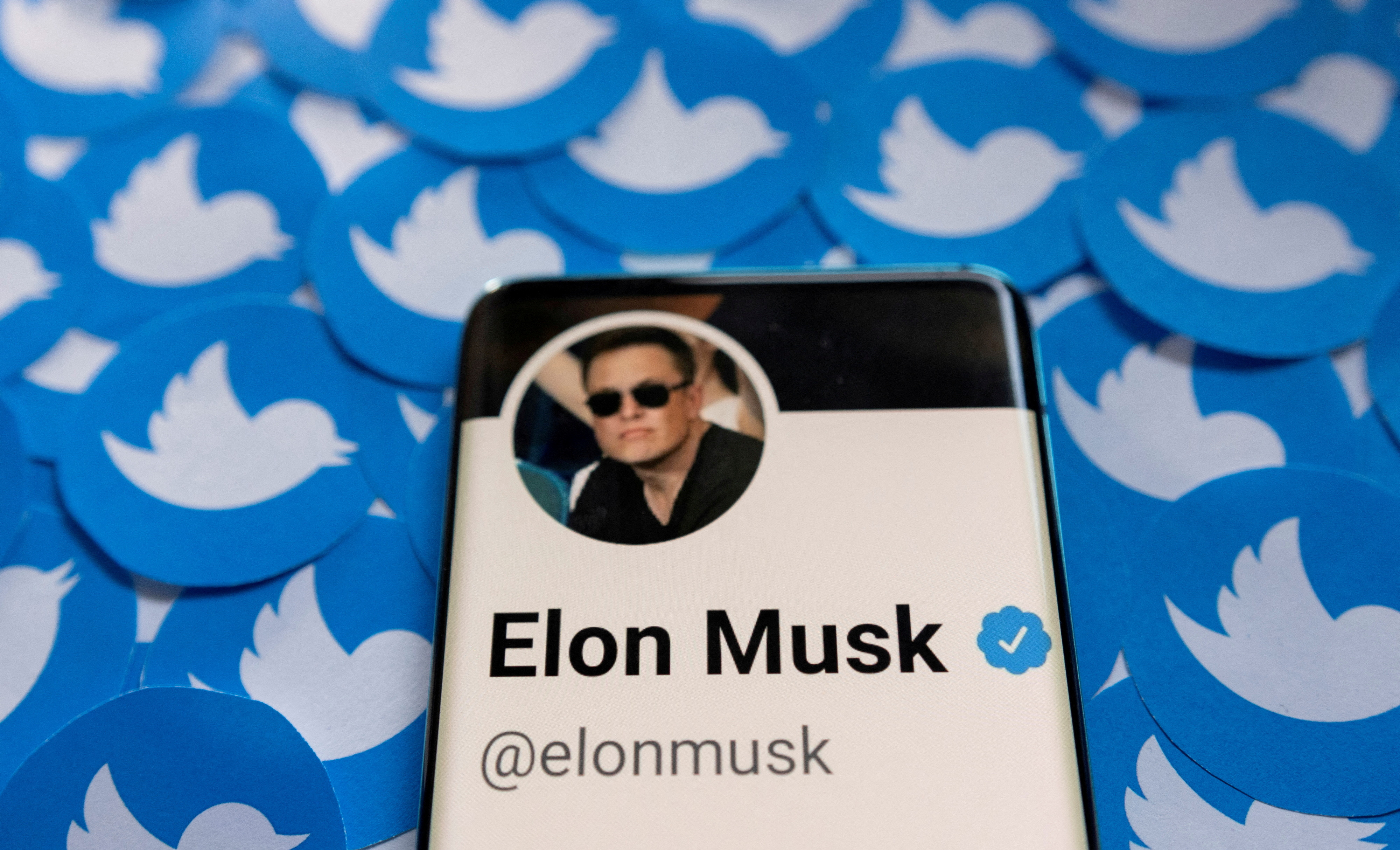 Elon Musk's Twitter profile is seen on a smartphone placed on printed Twitter logos.
