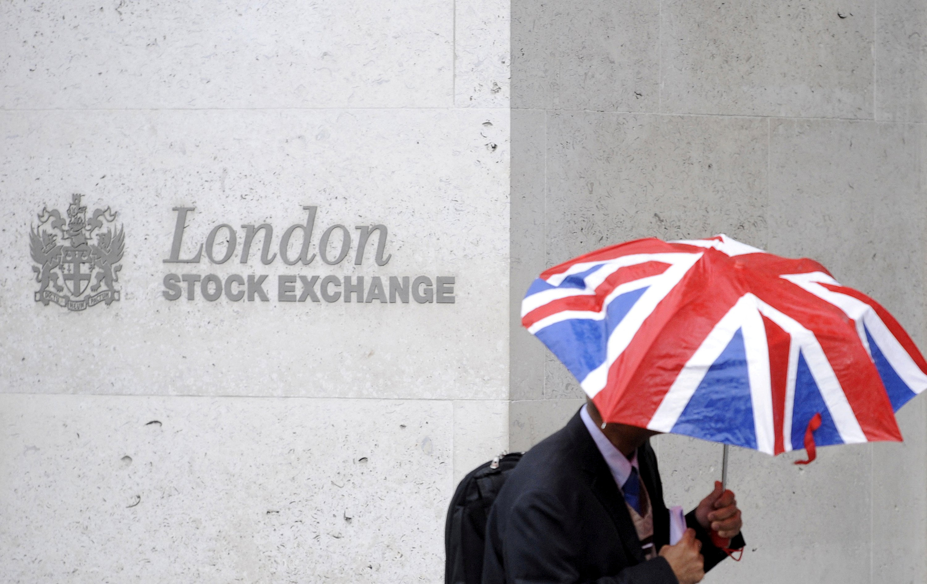 A worker shelters from the rain under a Union Flag umbrella as he passes the London Stock Exchange in London