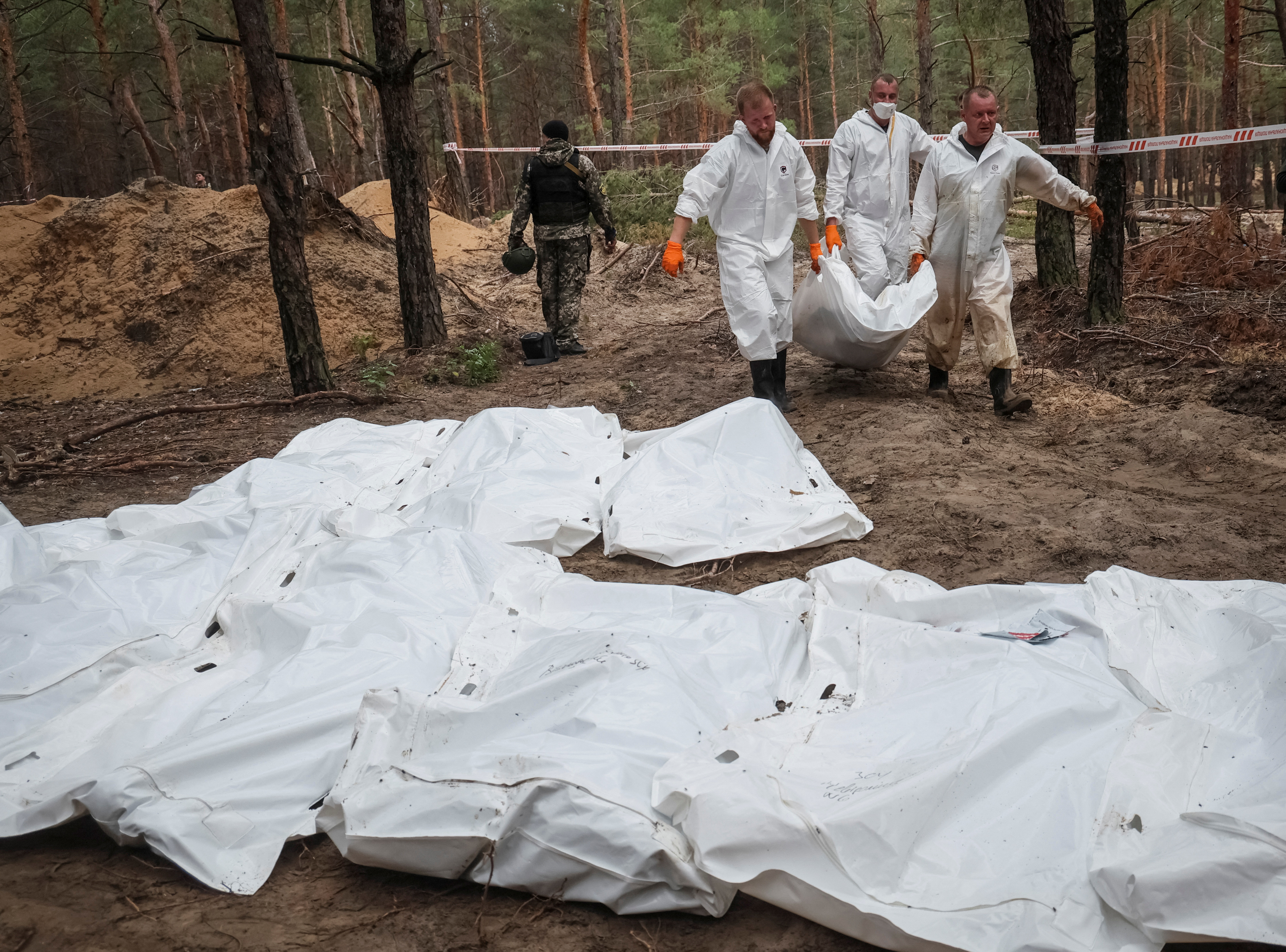 Experts carry a body as they work at a mass burial site in the town of Izium, recently liberated by Ukrainian Armed Forces, in Kharkiv region, Ukraine, on September 16, 2022 [Gleb Garanich/Reuters]