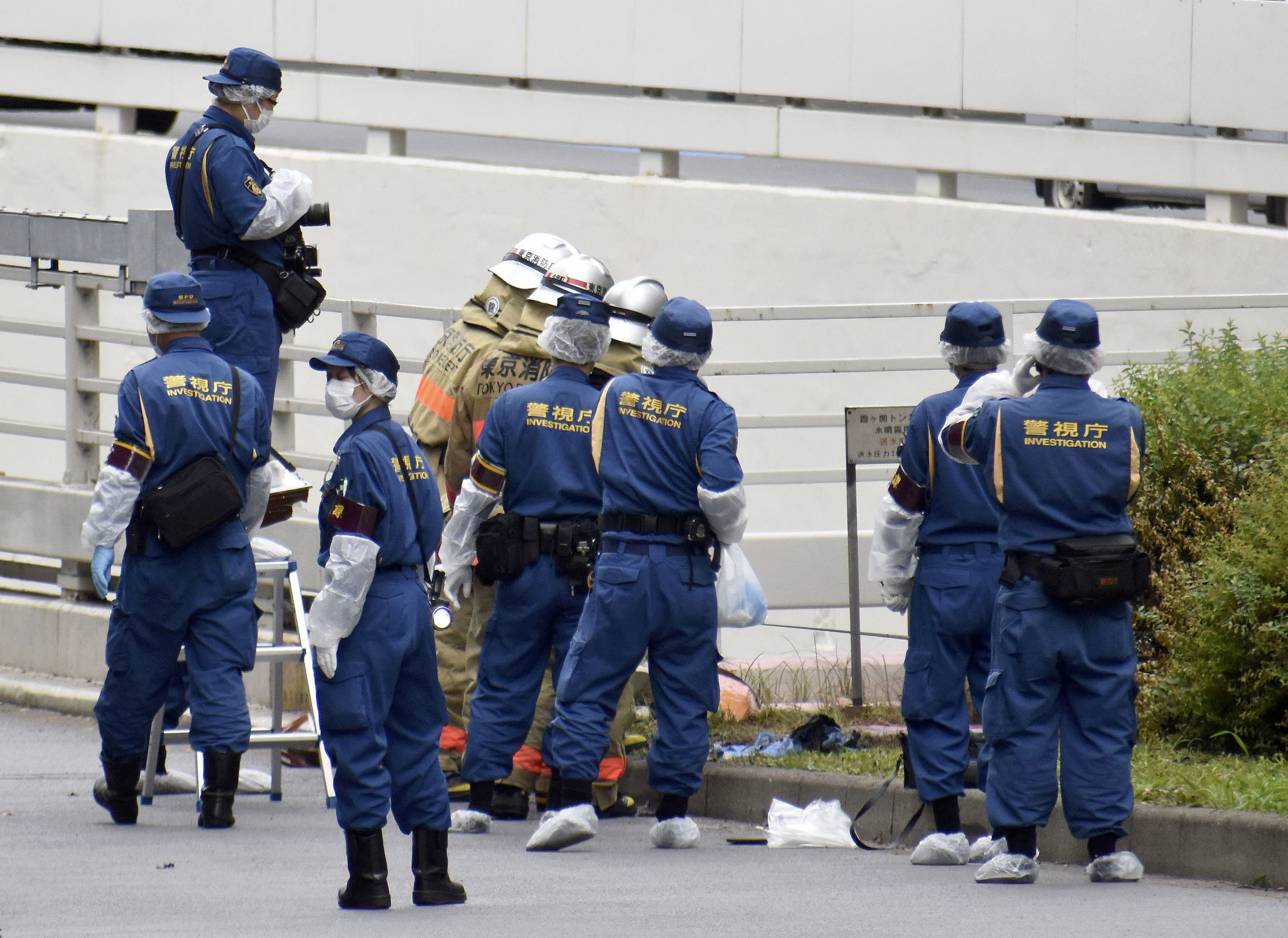 Police officers in blue overalls with 'investigator' written on the back work at the site where a man set himself on fire near the prime minister's office in Tokyo, Japan.