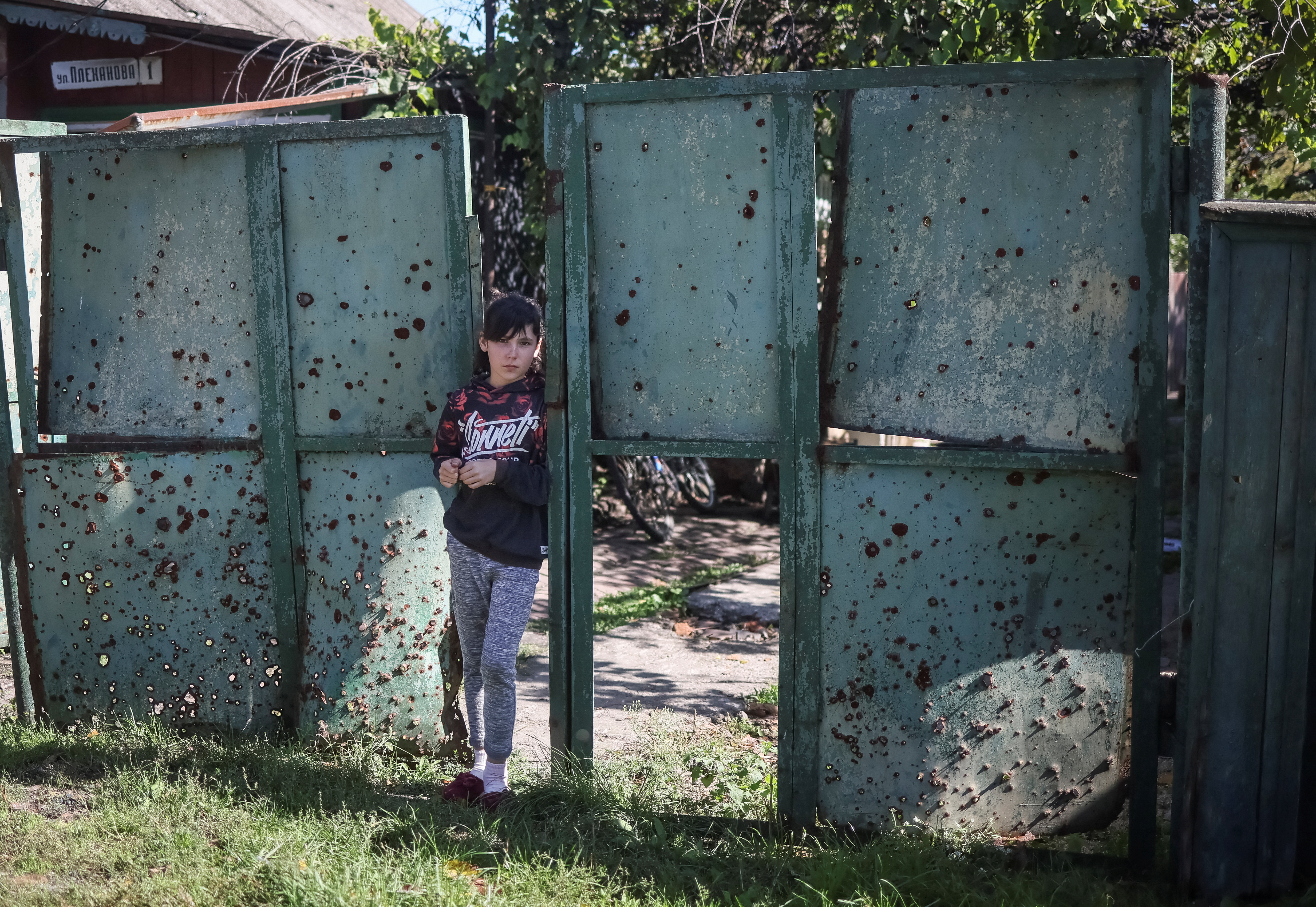 A ukrainian girl stands on a gate with holes created by shrapnel near her house, as Russia's attack on Ukraine continues, in the village of Savyntsi, recently liberated by Ukrainian Armed Forces, in Kharkiv region, Ukraine September 21, 2022. REUTERS/Gleb Garanich