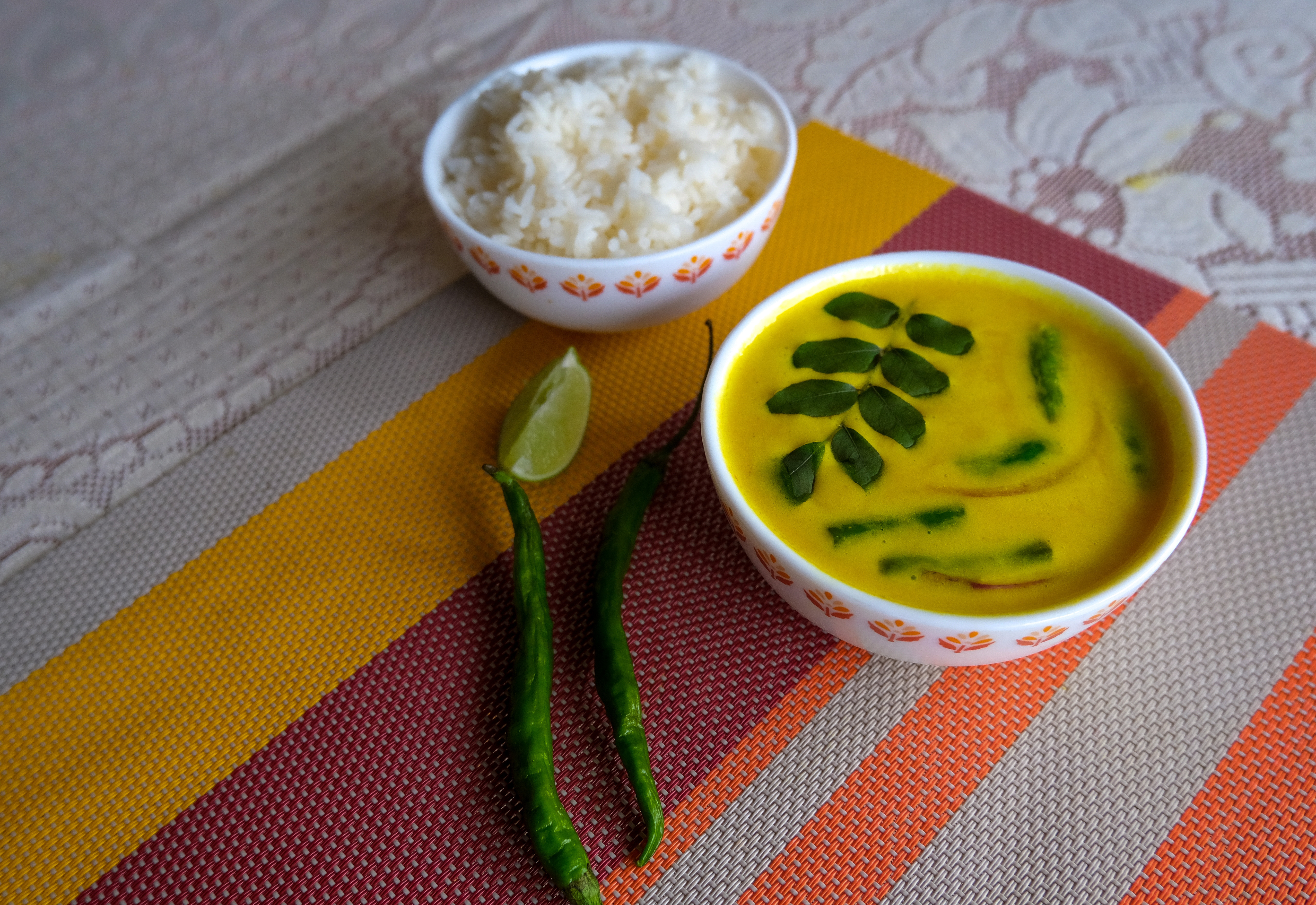 A bowl of rice sits next to a bowl of diya bath toppings