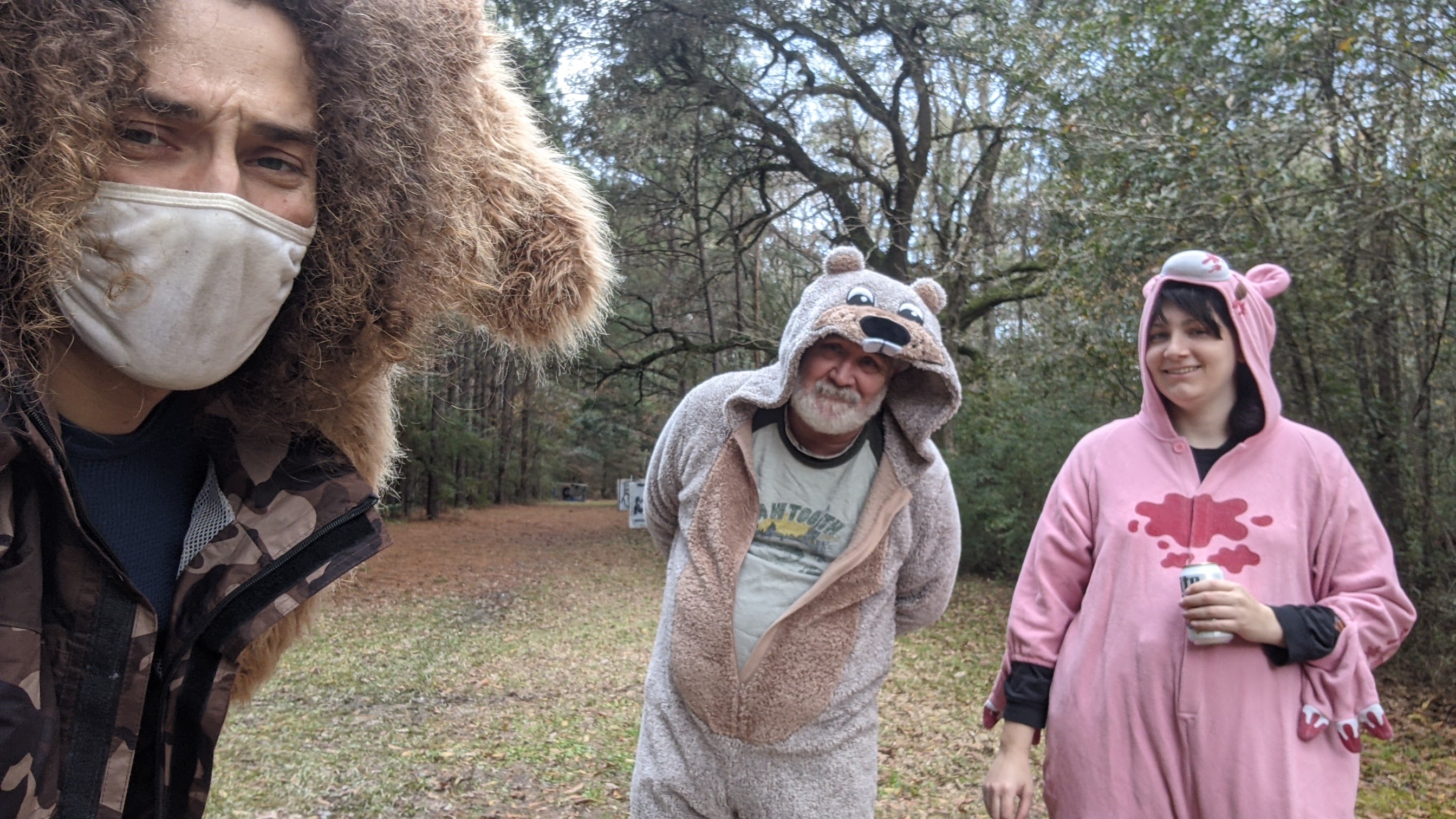 A photo of three people, one taking a selfie and two other people wearing one piece pyjamas/costumes.