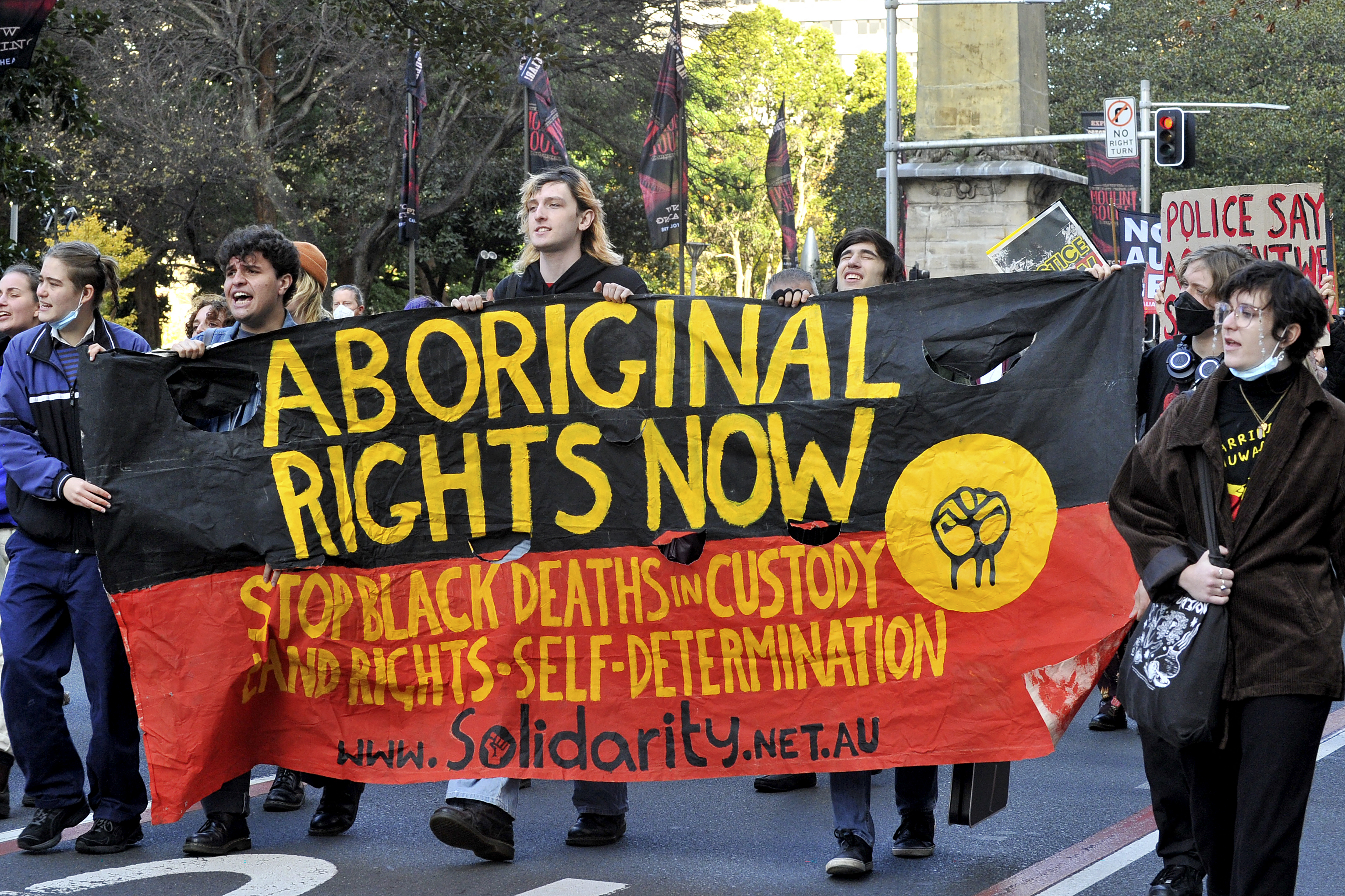 Protesters walk with a banner in the colours of the Aboriginal flag reading 'Aboriginal rights now'