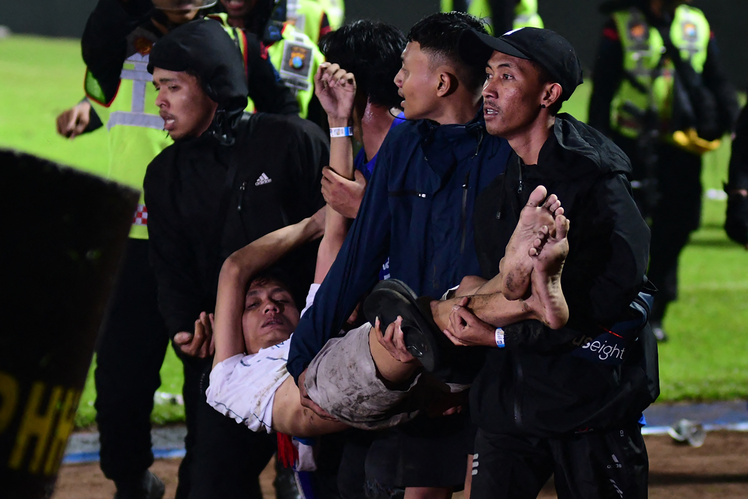 In this picture taken on October 1, 2022, a group of people carry a man after a football match between Arema FC and Persebaya Surabaya at Kanjuruhan stadium in Malang