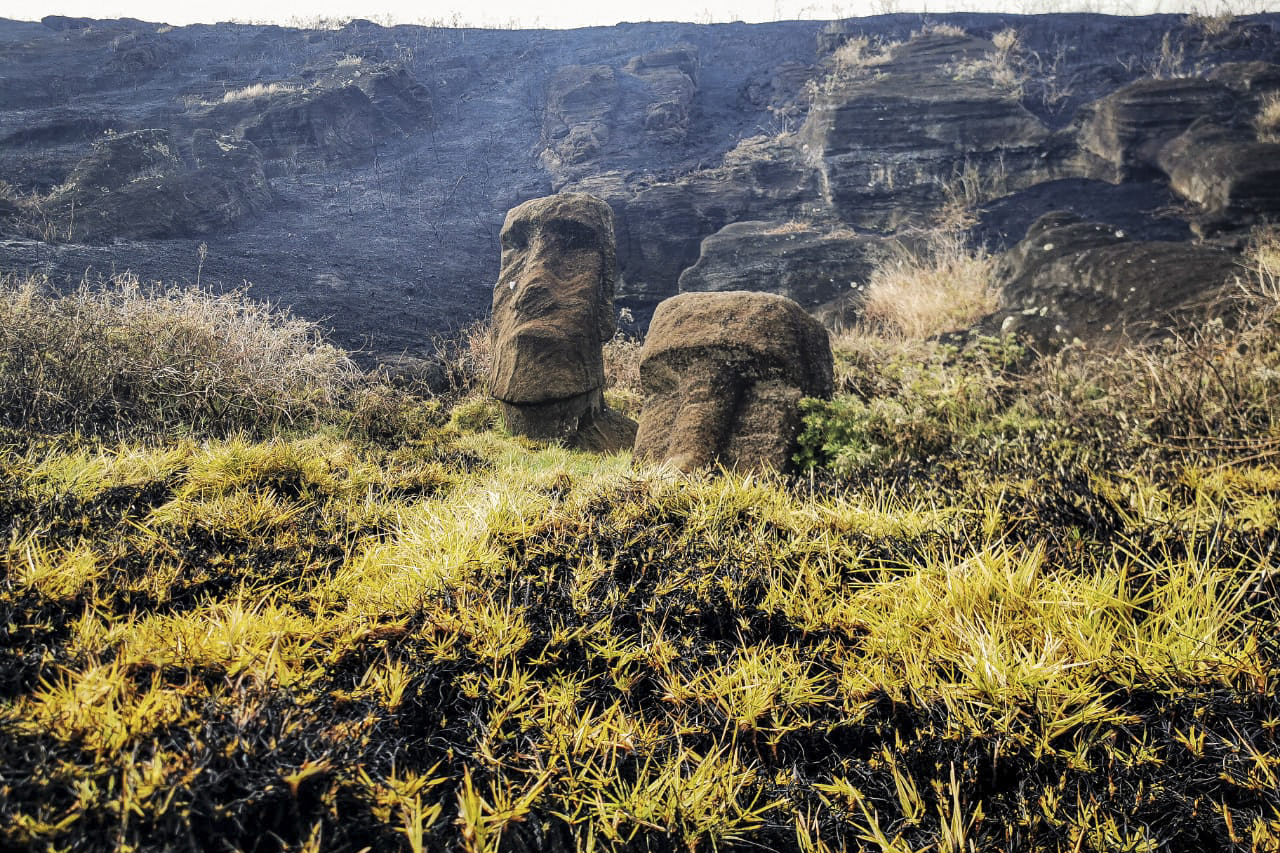 Moai stone statues are seen as smoke rises behind them.