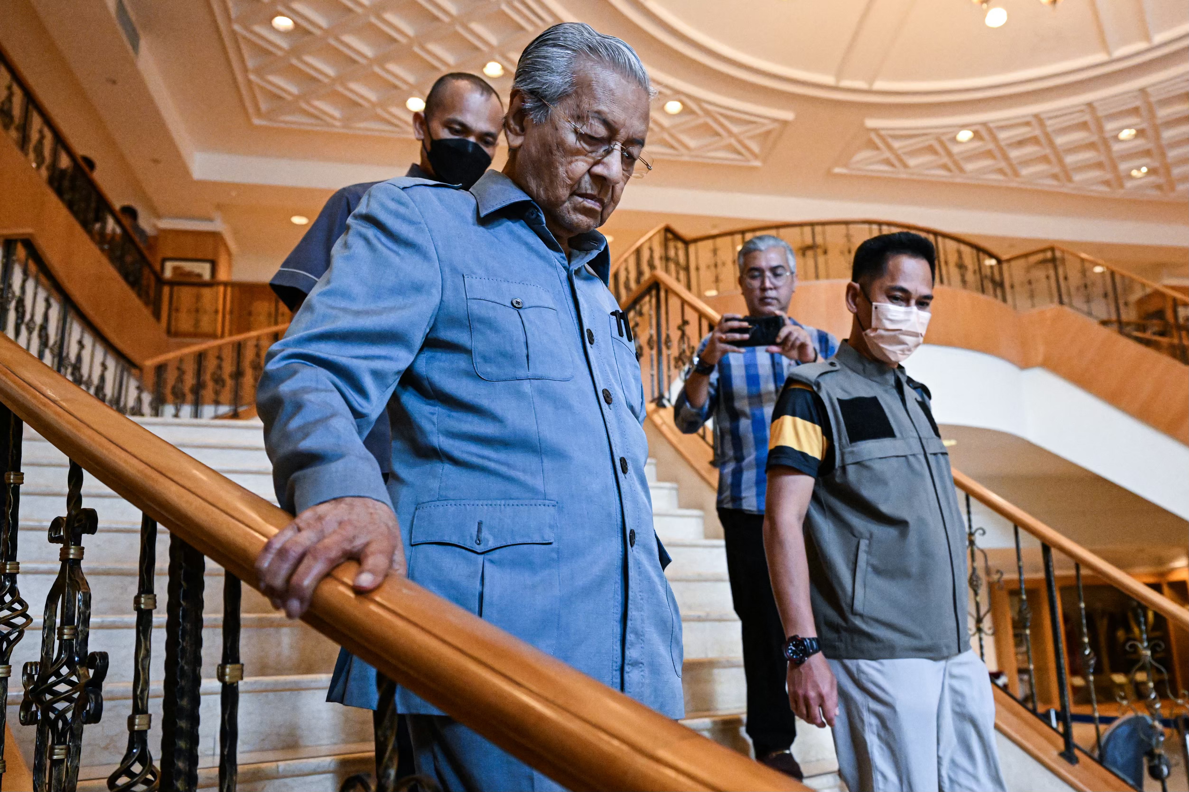 Mahathir Mohamad in blue suit walks down the staircase at his foundation in Putrajaya