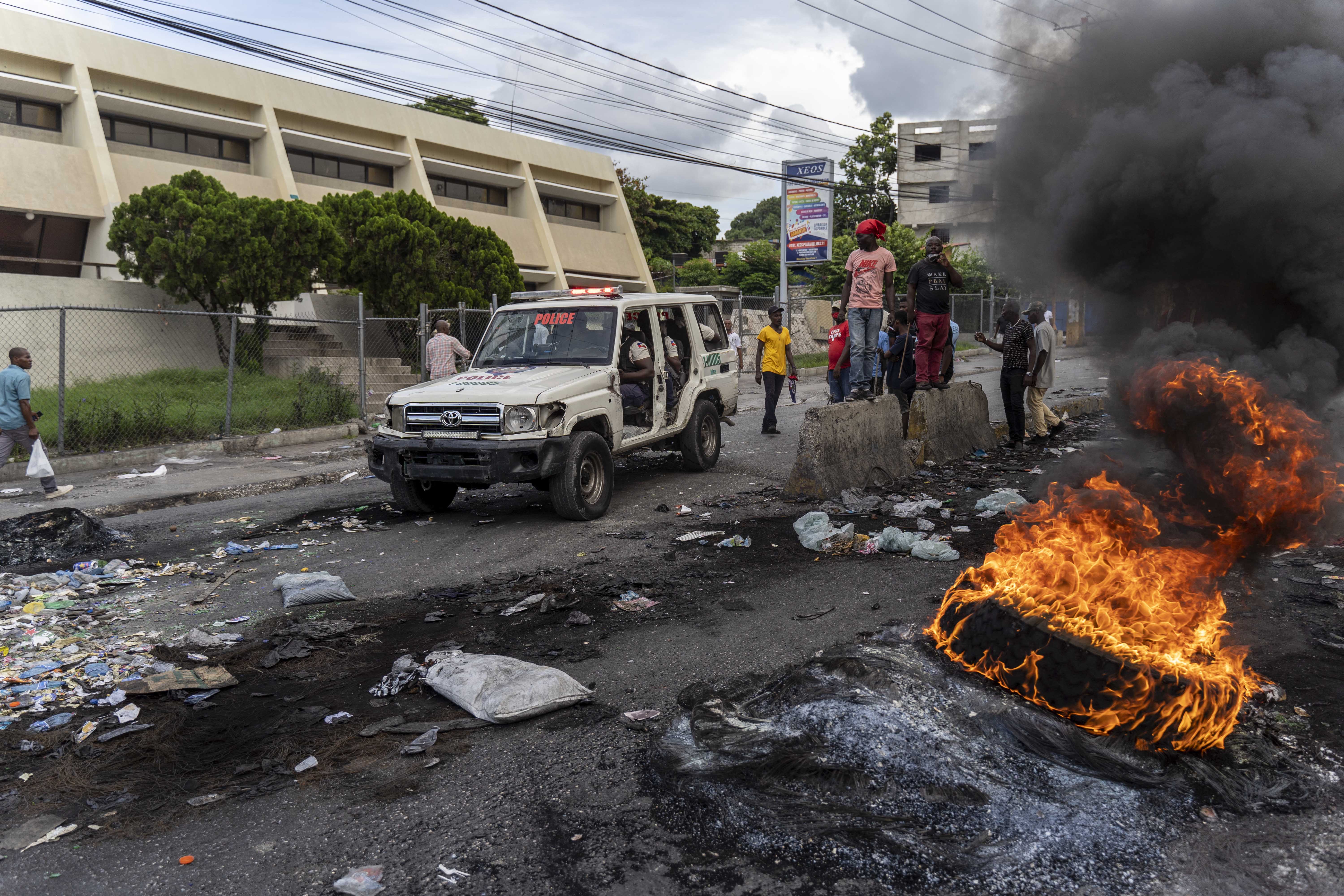 A car drives by burning tyres during a demonstration in Haiti