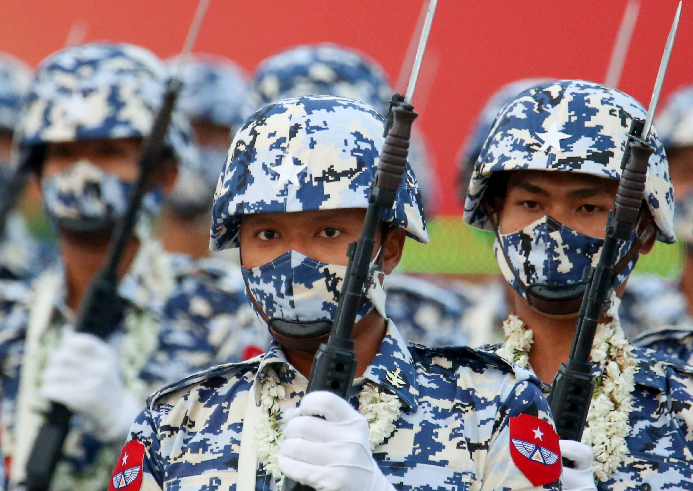 Close up of several men in camouflage gear holding up rifles with attached bayonets.
