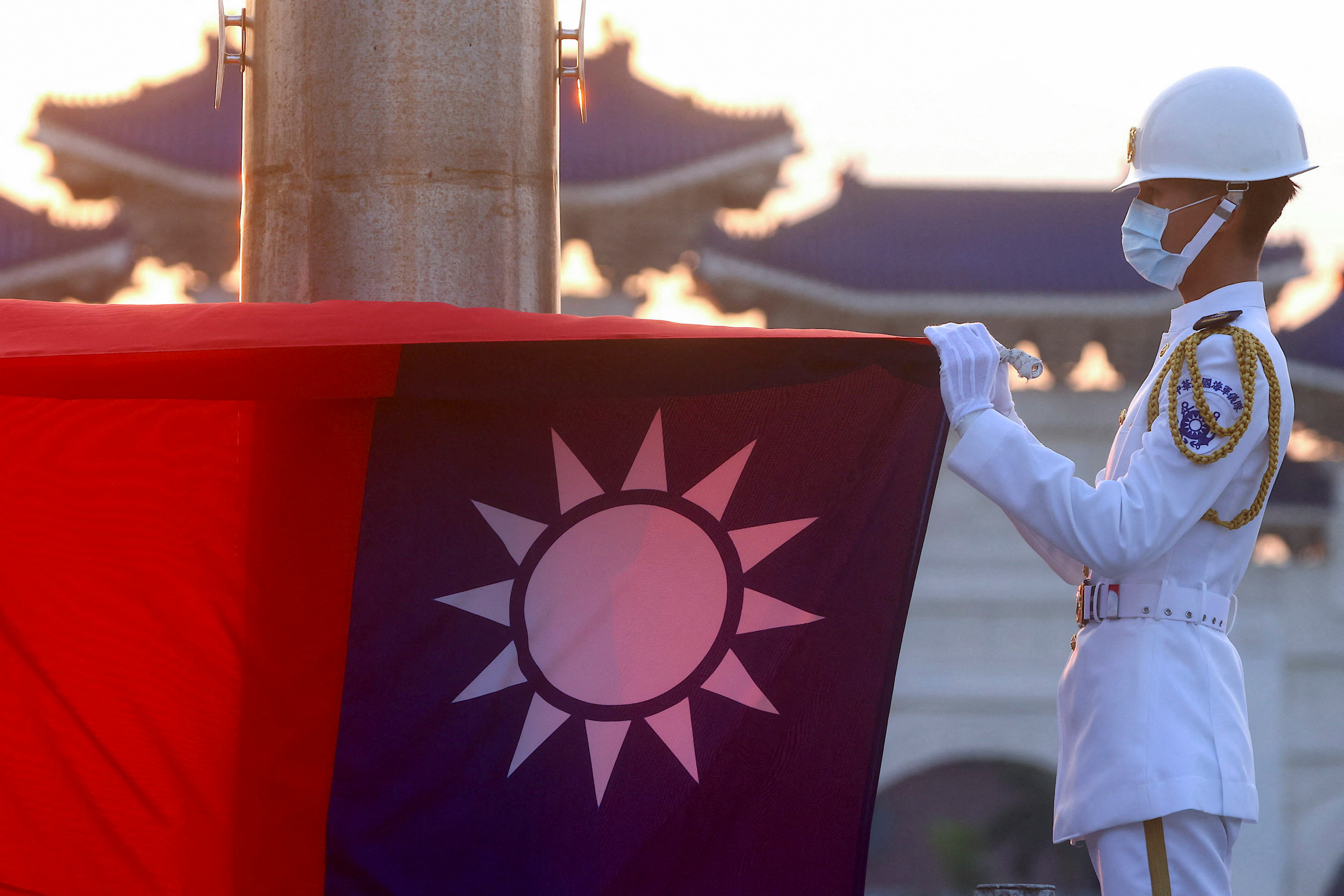 Profile of guard in white uniform and hat and lowered red and blue flag