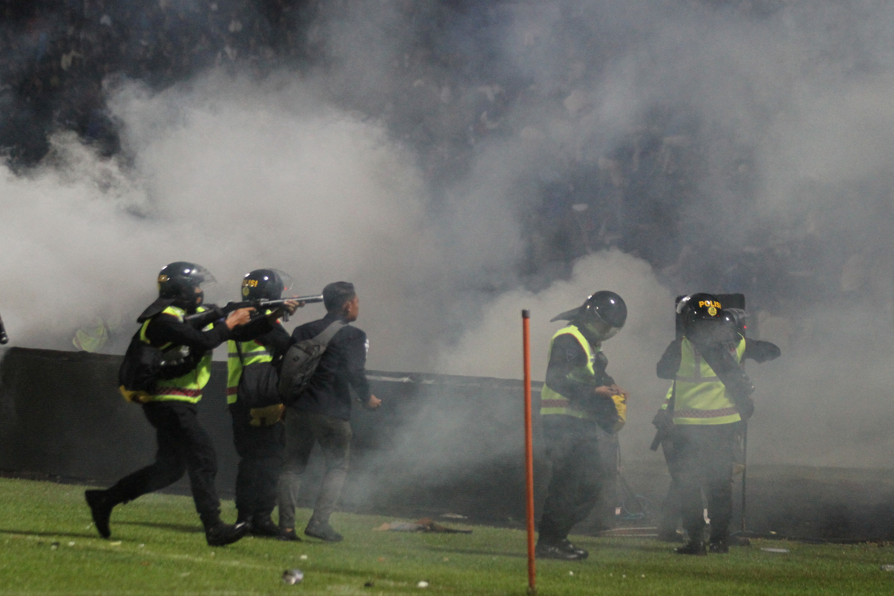 Indonesia police fire off clouds of tear gas as they stand on the pitch after Arema vs Persebaya at Kanjuruhan Stadium.
