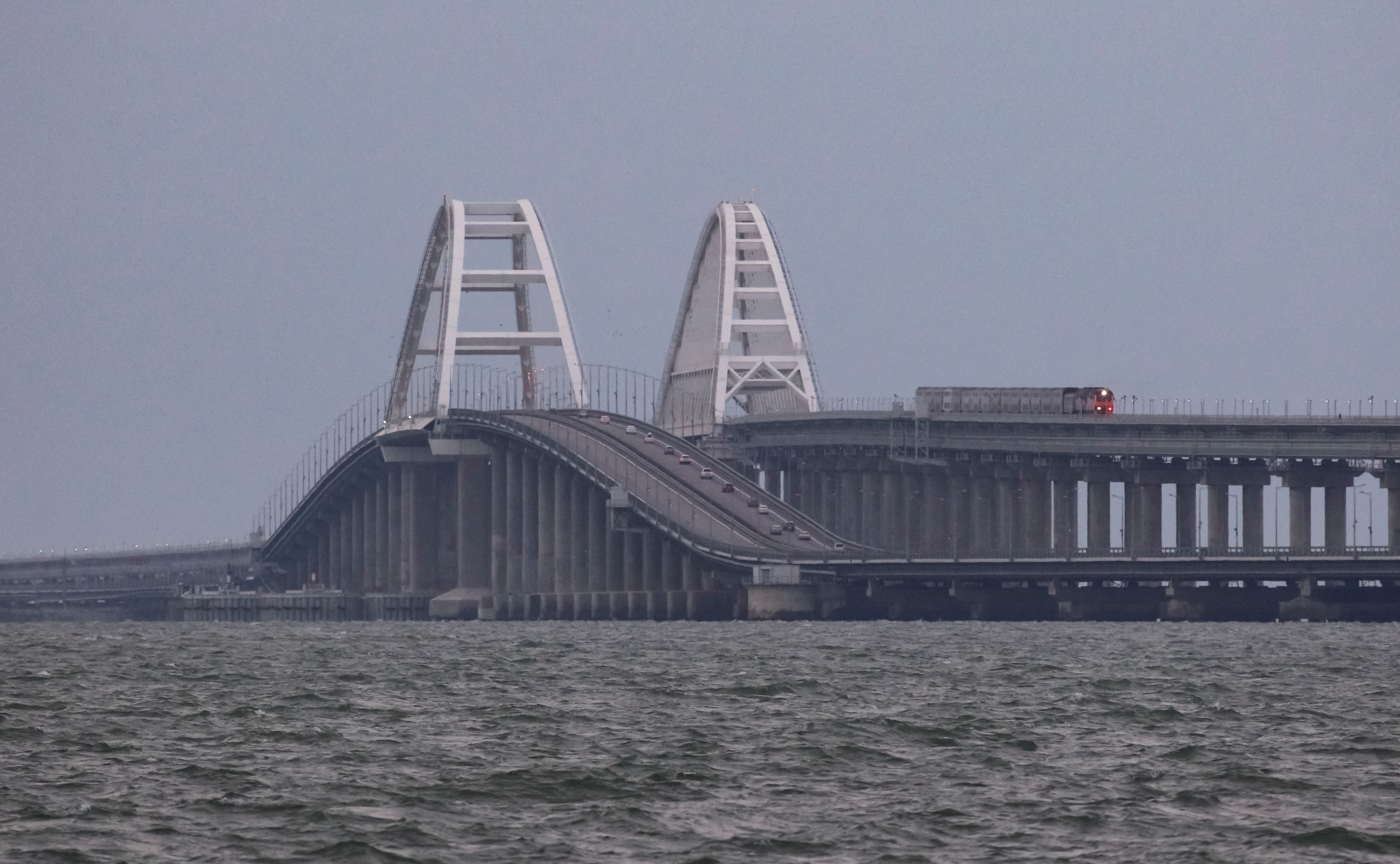 A passenger train and cars drive on the Kerch bridge, after an explosion destroyed part of it, in the Kerch Strait, Crimea, October 9, 2022.