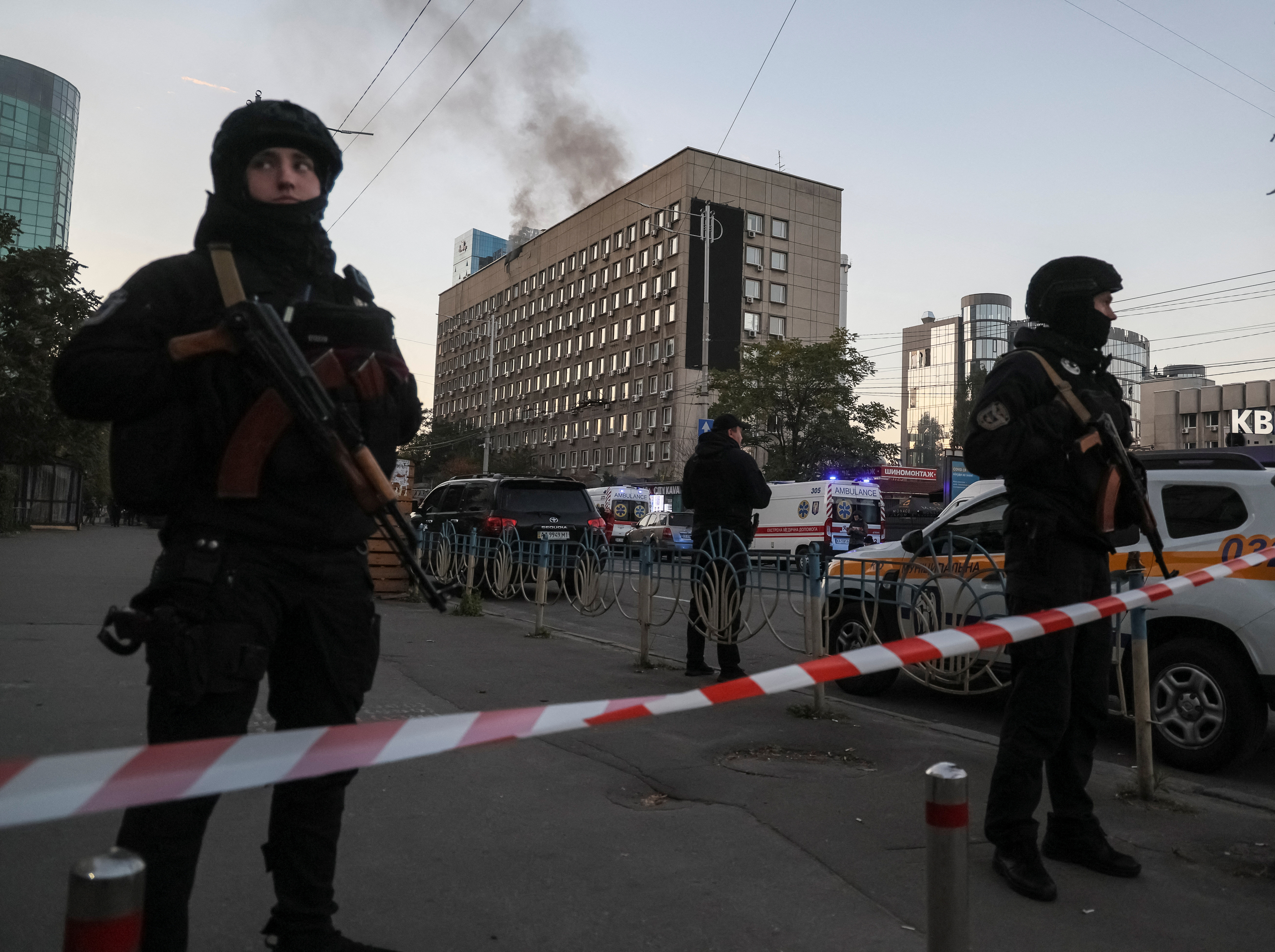 Soldiers stand behind police tape as smoke rises from a building behind them
