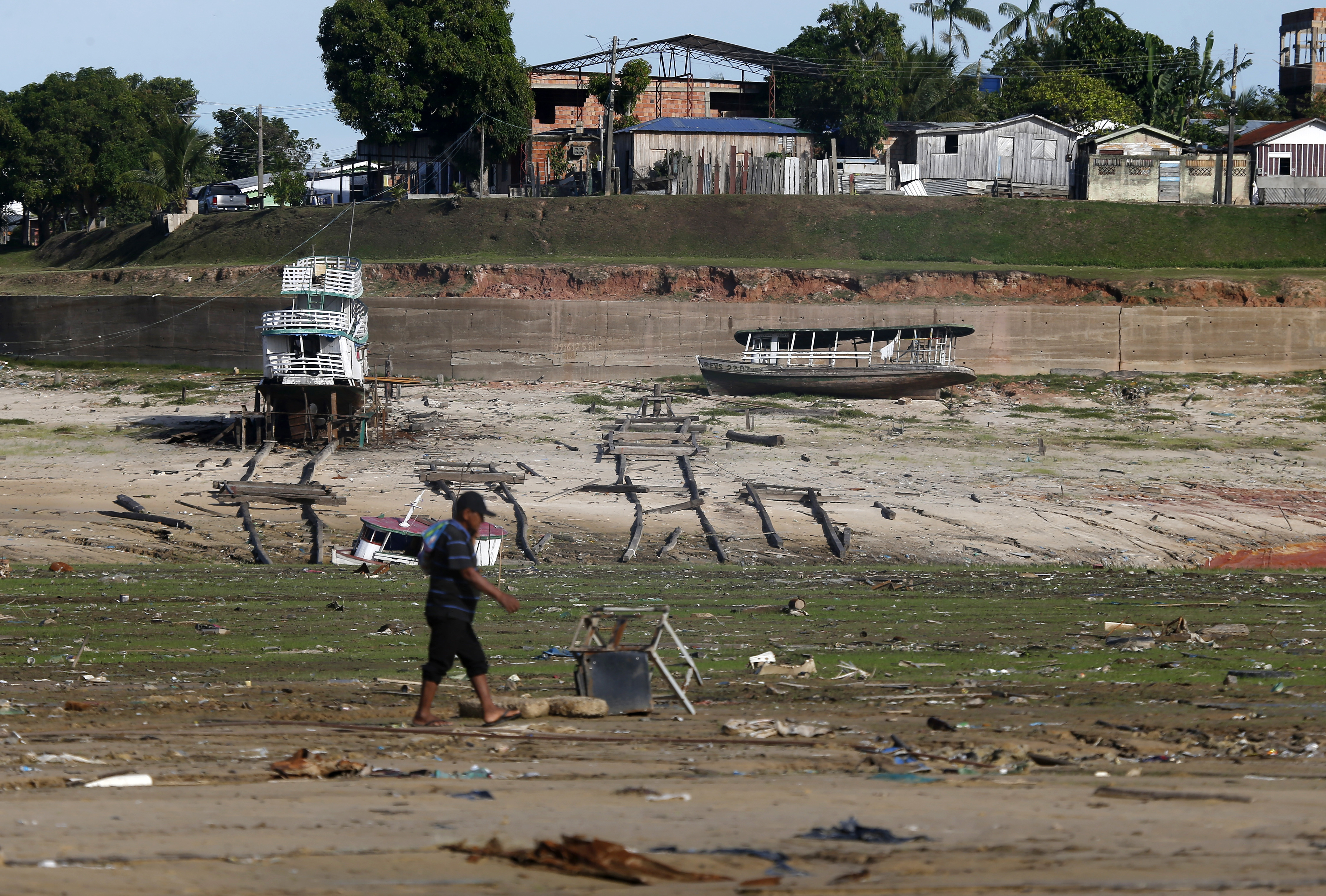 A man walks by boats on dry land in an area impacted by the drought near the Solimões River, in Tefe, Amazonas state, Brazil