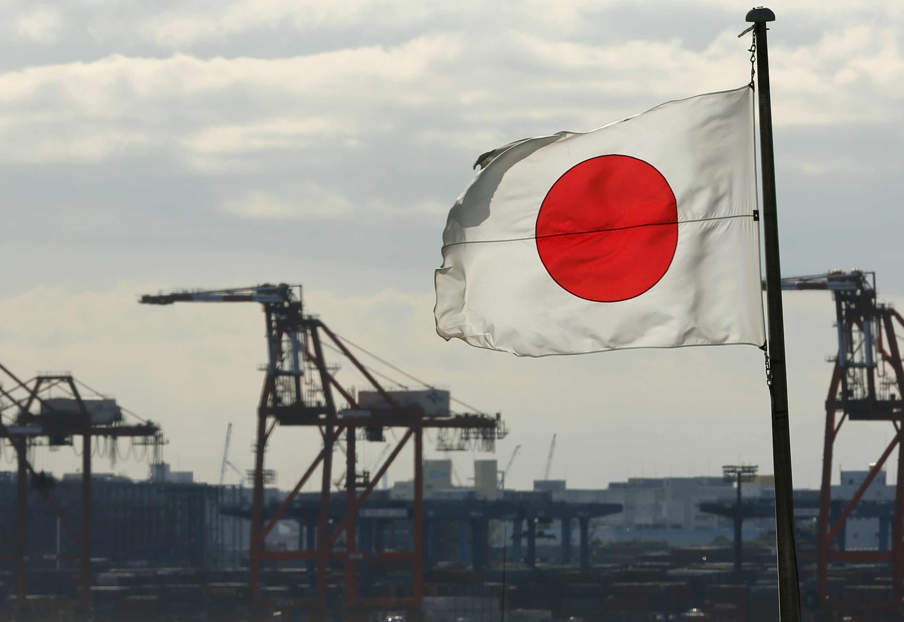 A Japanese flag flutters in front of a shipping container area, at a port in Tokyo, Japan.