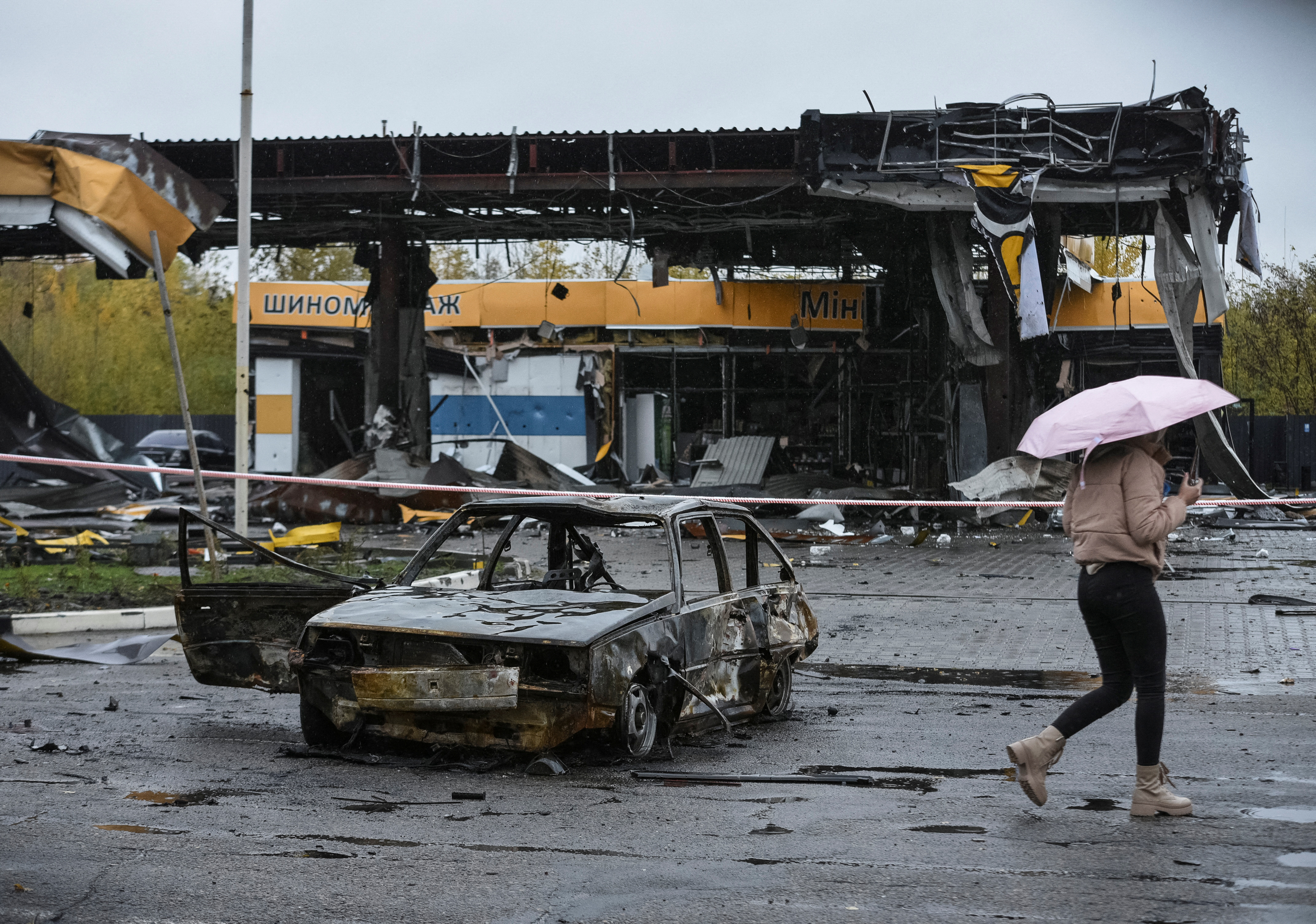 A woman passes by a gas station destroyed by Russian military strike