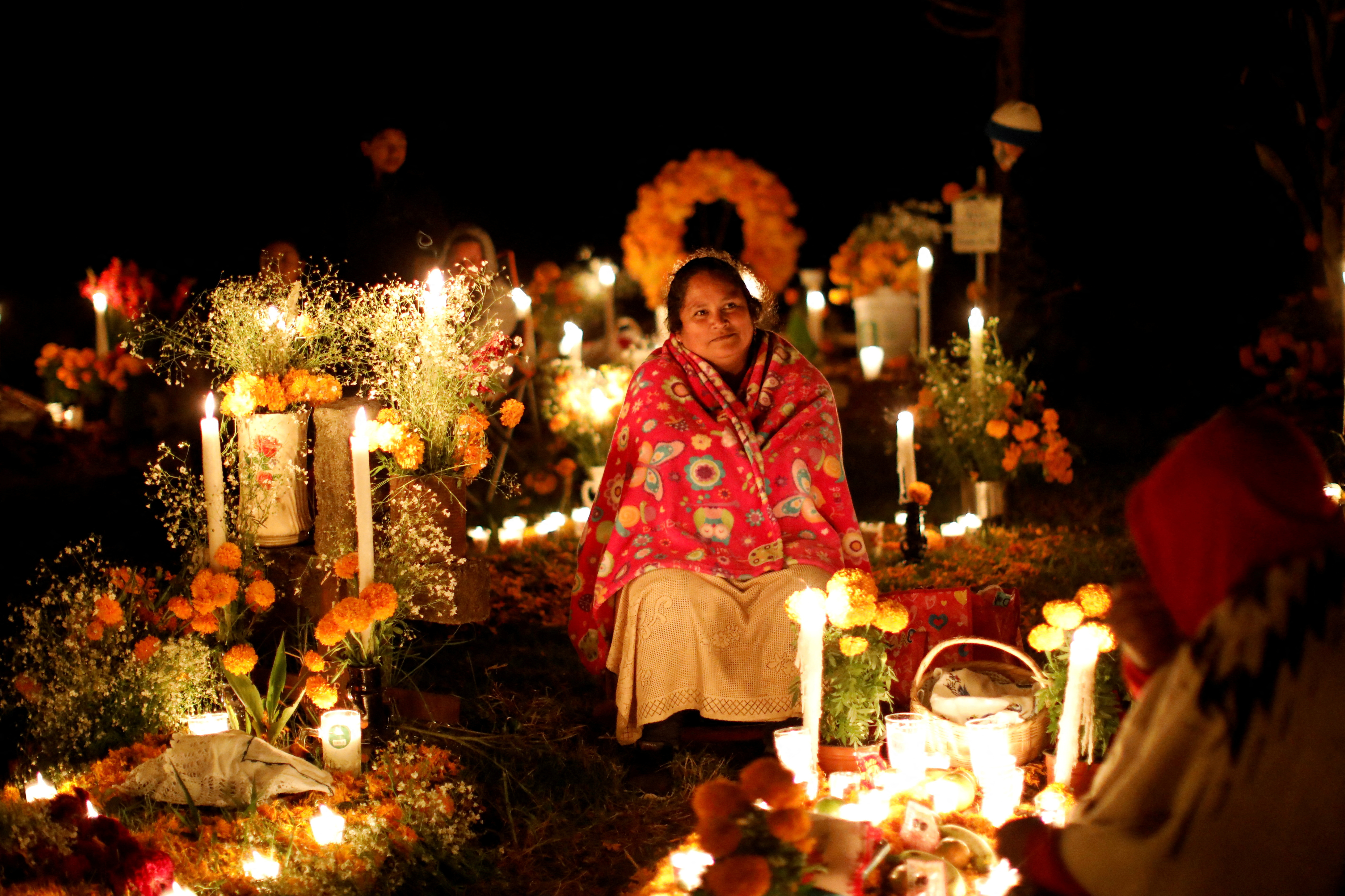 A woman sits next to a grave during the Day of the Dead