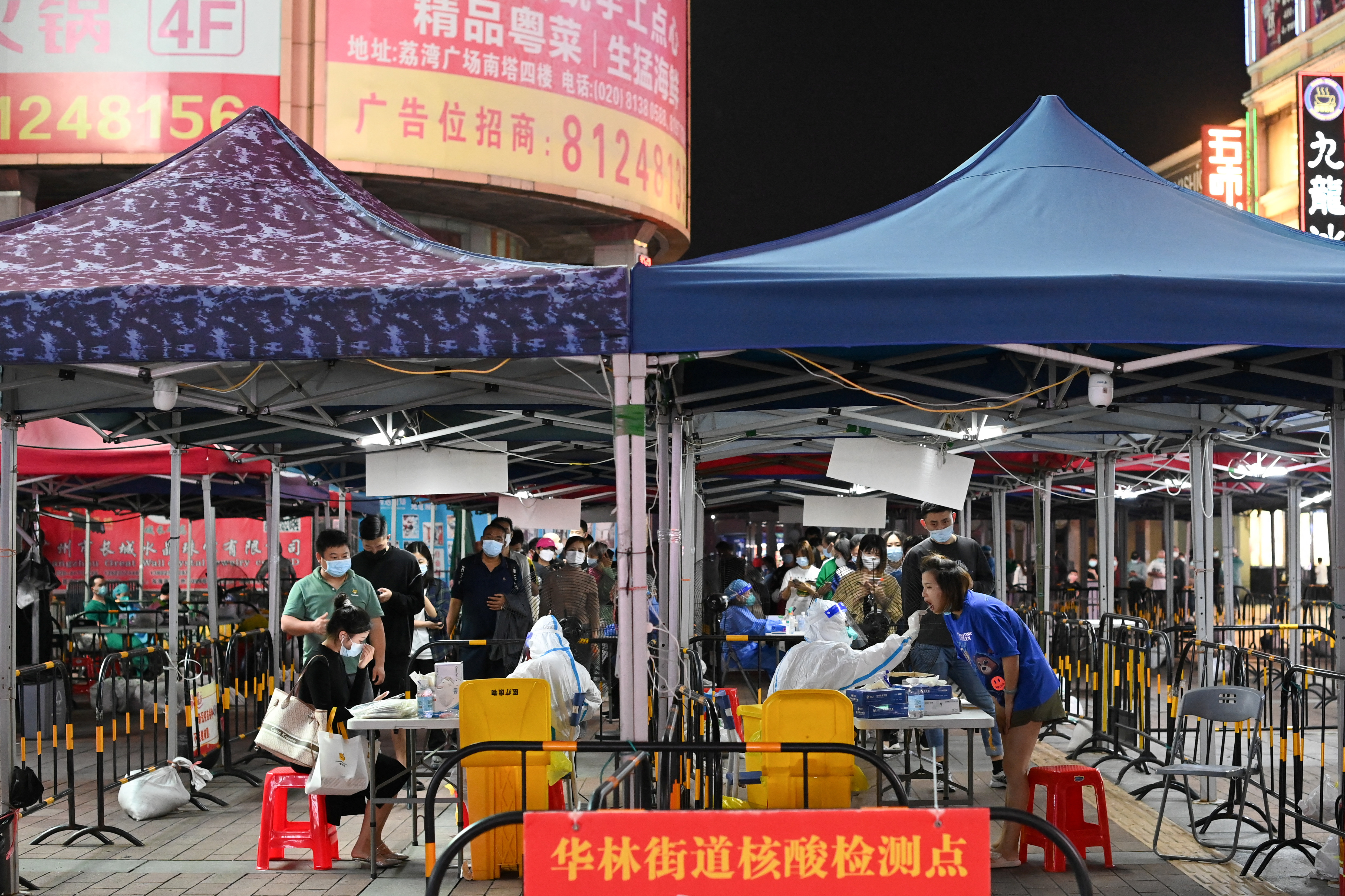 Masked people lining up for COVID-19 tests beneath blue canopies in Guangzhou