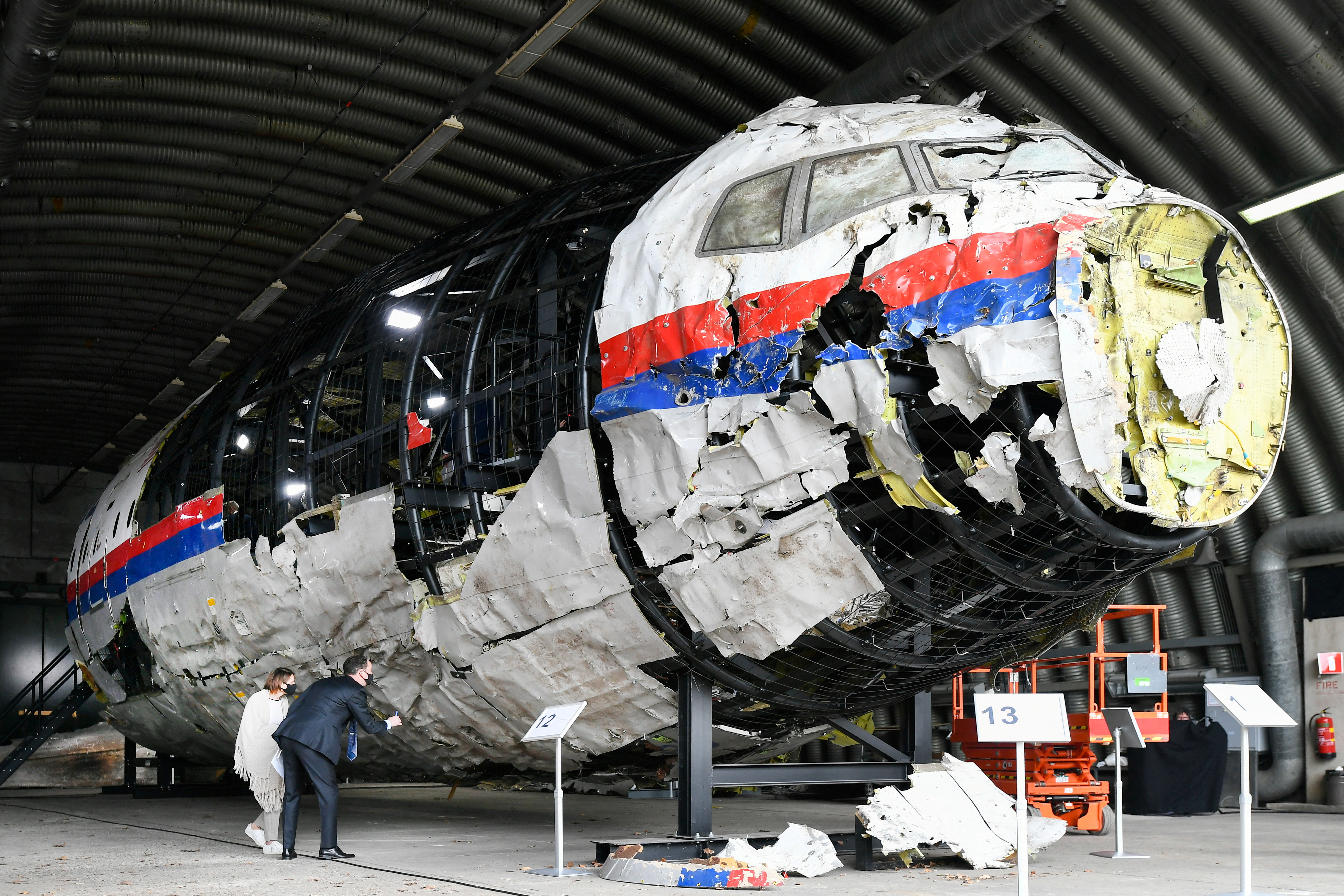 Front of wrecked white aeroplane with red and blue stripes, propped up in warehouse