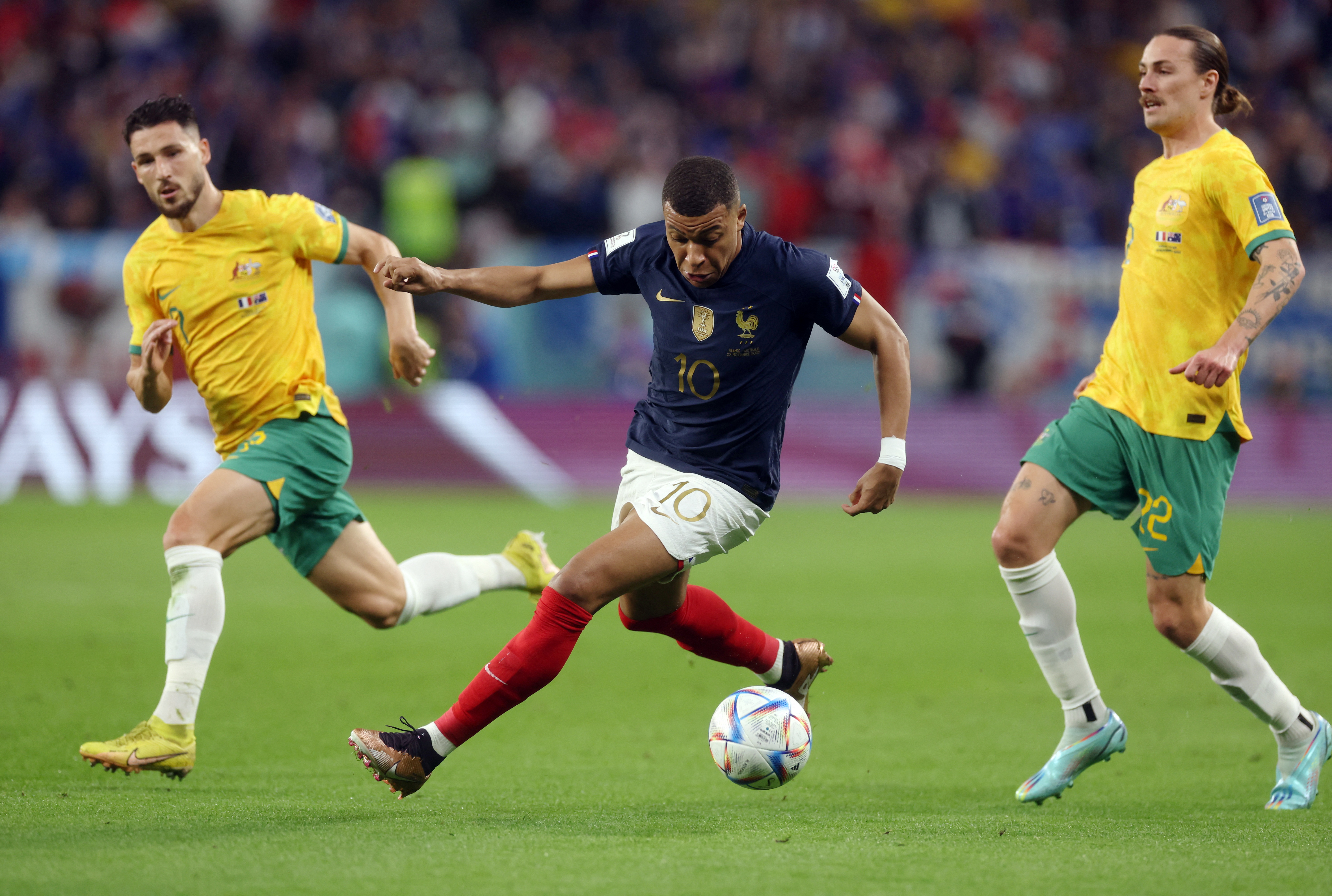 Mbappe kicking a ball with Australian players on each side of him