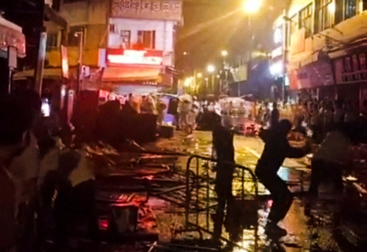 Protesters - silhouetted against lights - throw things at the police on a street in Guangzhou. There are barriers, and neon shop signs in the background
