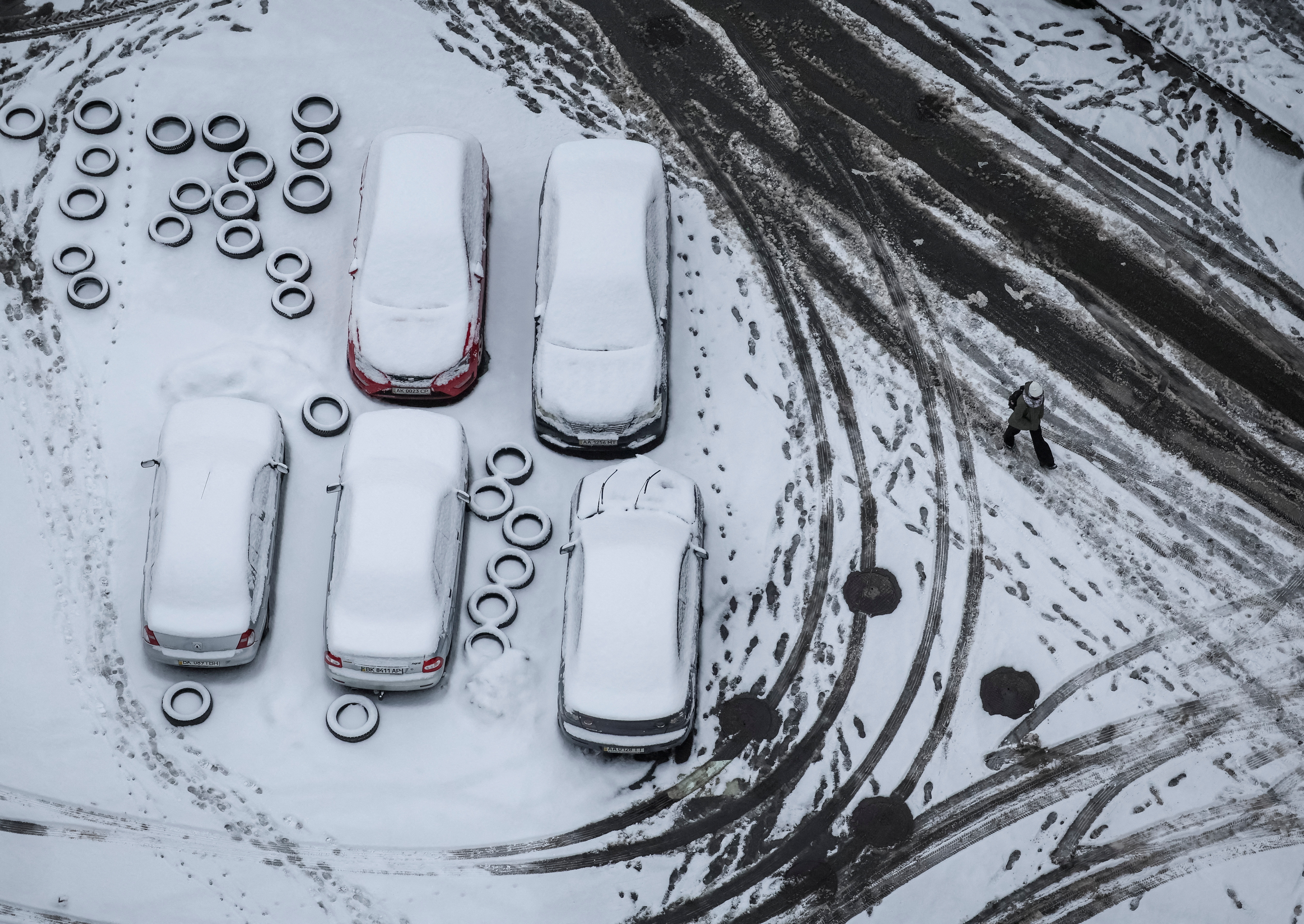 A pedestrian passes by cars covered in snow, in Kyiv, Ukraine November 30, 2022. REUTERS/Gleb Garanich TPX IMAGES OF THE DAY