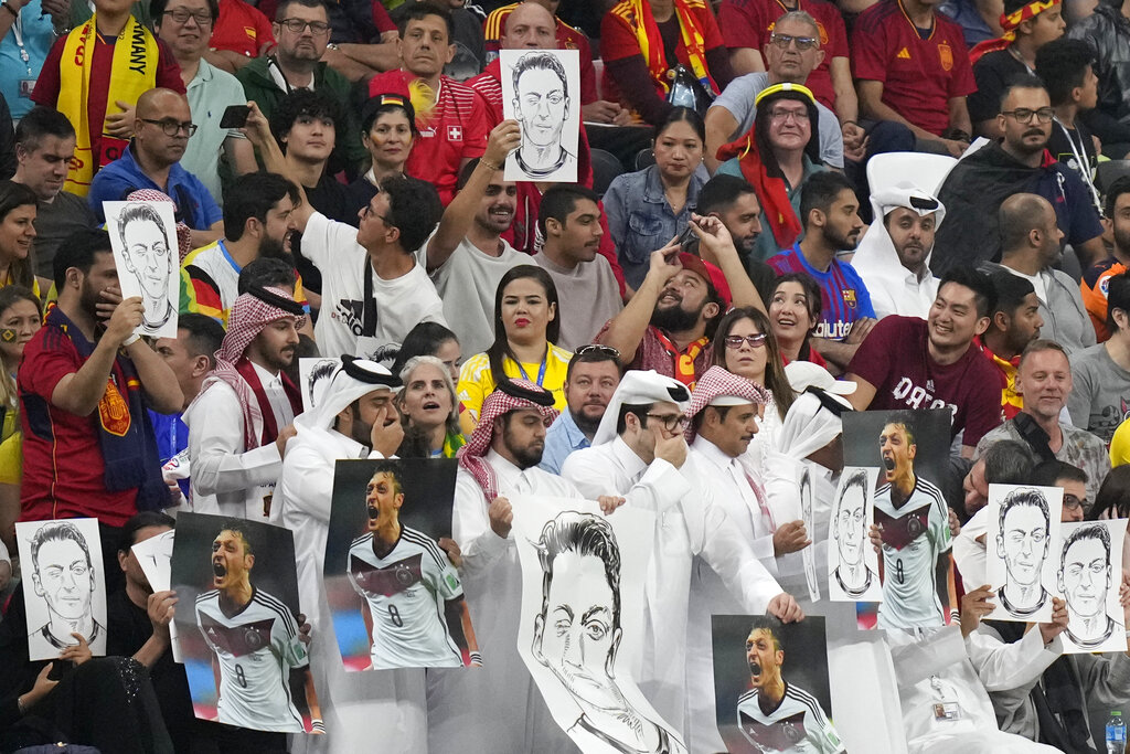 Spectators hold photos of former German international player Mesut Ozil on the stands and cover their mouths during the World Cup group E football match between Spain and Germany at the Al Bayt Stadium in Al Khor , Qatar.