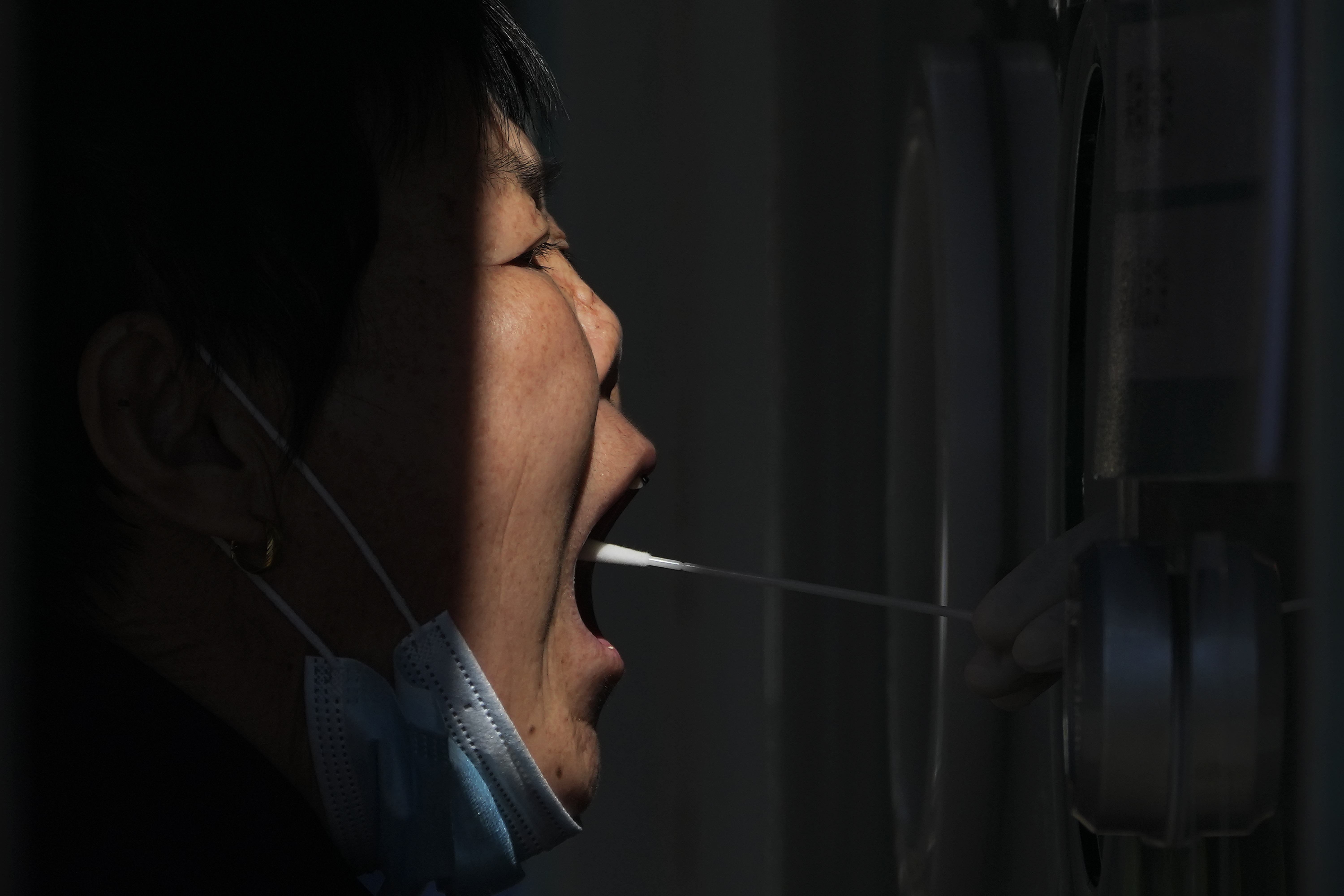 An older woman seen in profile having a swab taken from her throat.