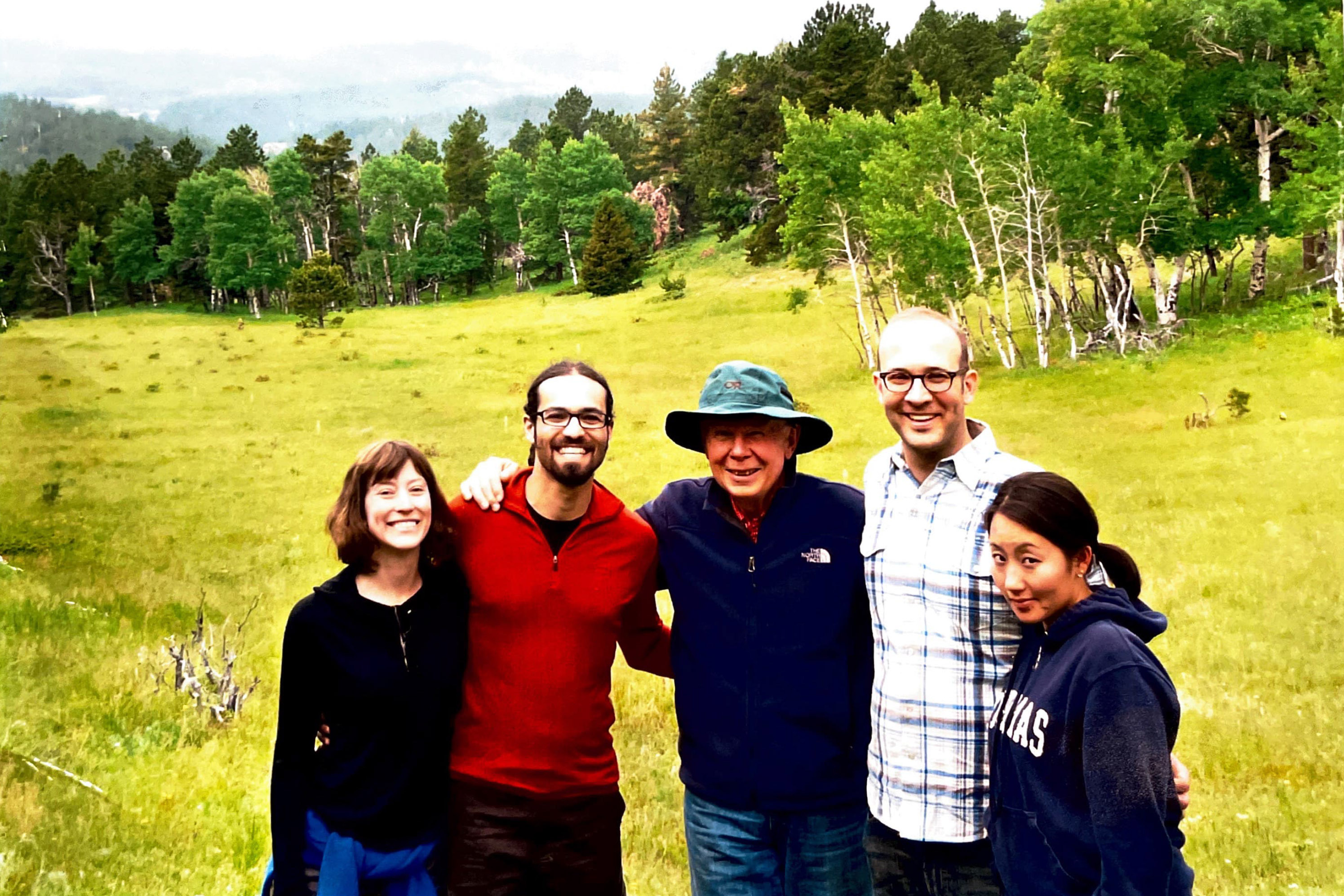 A photo of five people standing next to each other holding each others' shoulders.