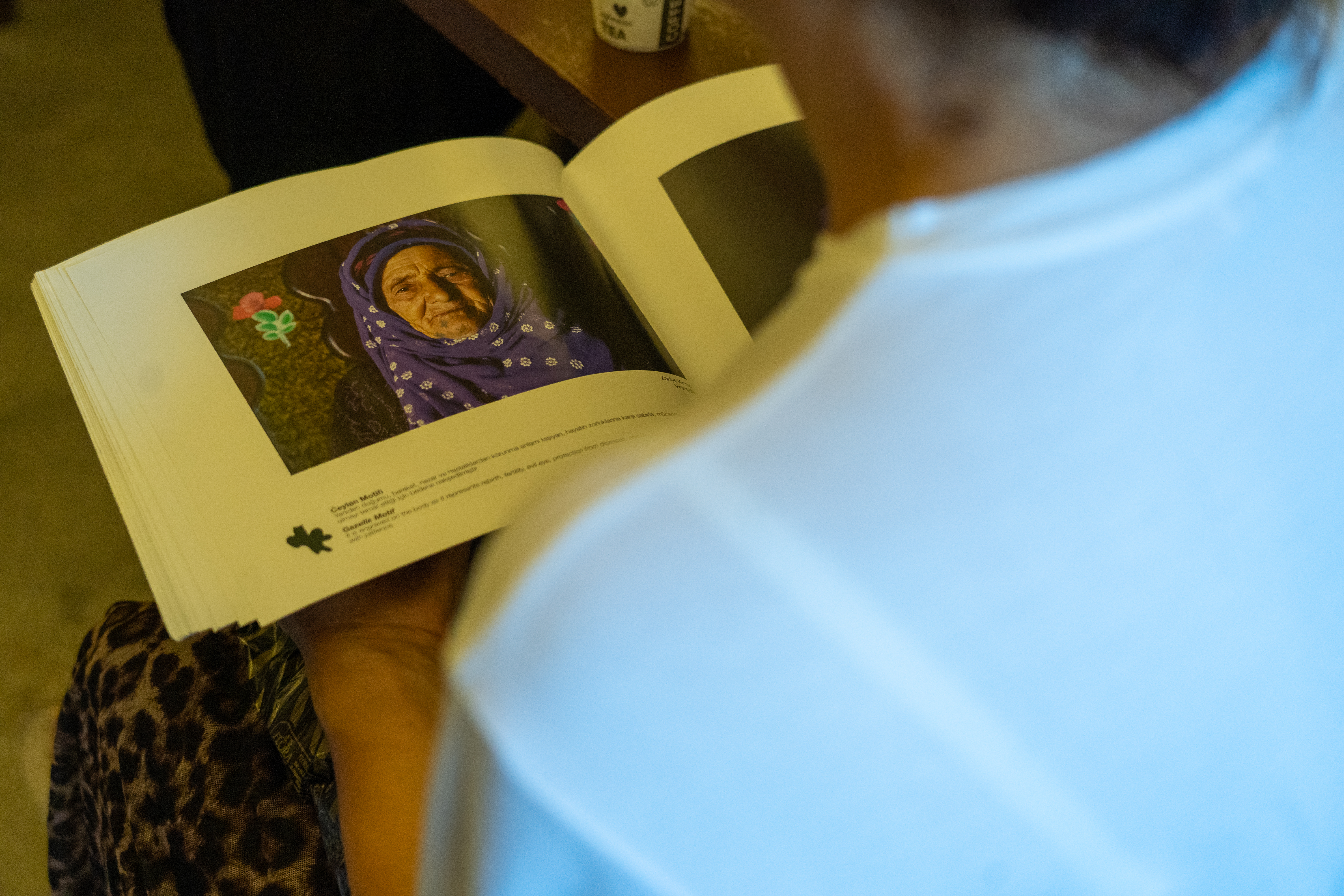 A photo of a customer in Temel’s studio perusing a book with numerous deq motifs and symbols, along with their meanings, still inked on elderly women and some men.