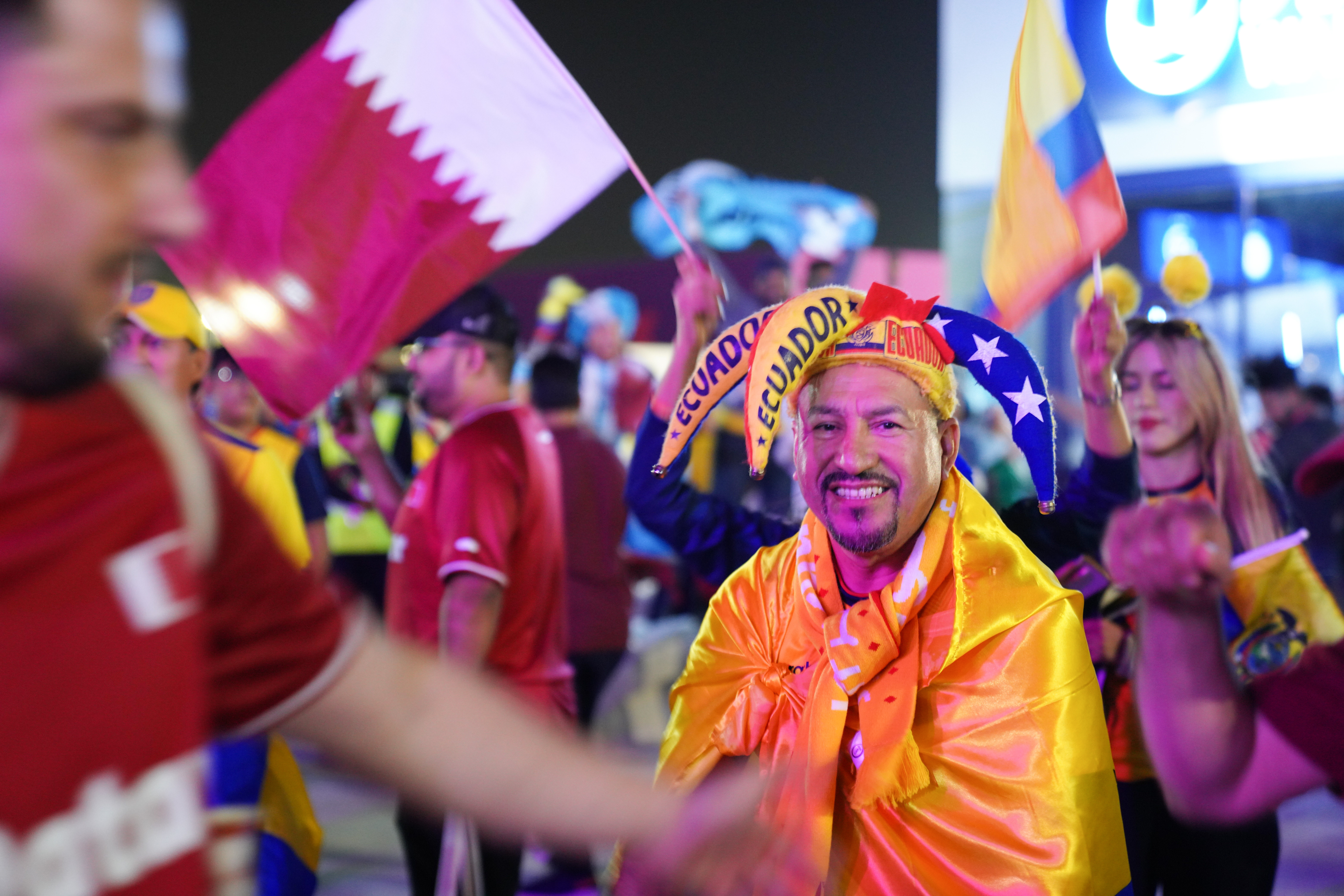 Ecuador fans celebrate outside Al Bayt stadium. One, wearing a jester's type hat with Ecuador colours, smiles at the camera
