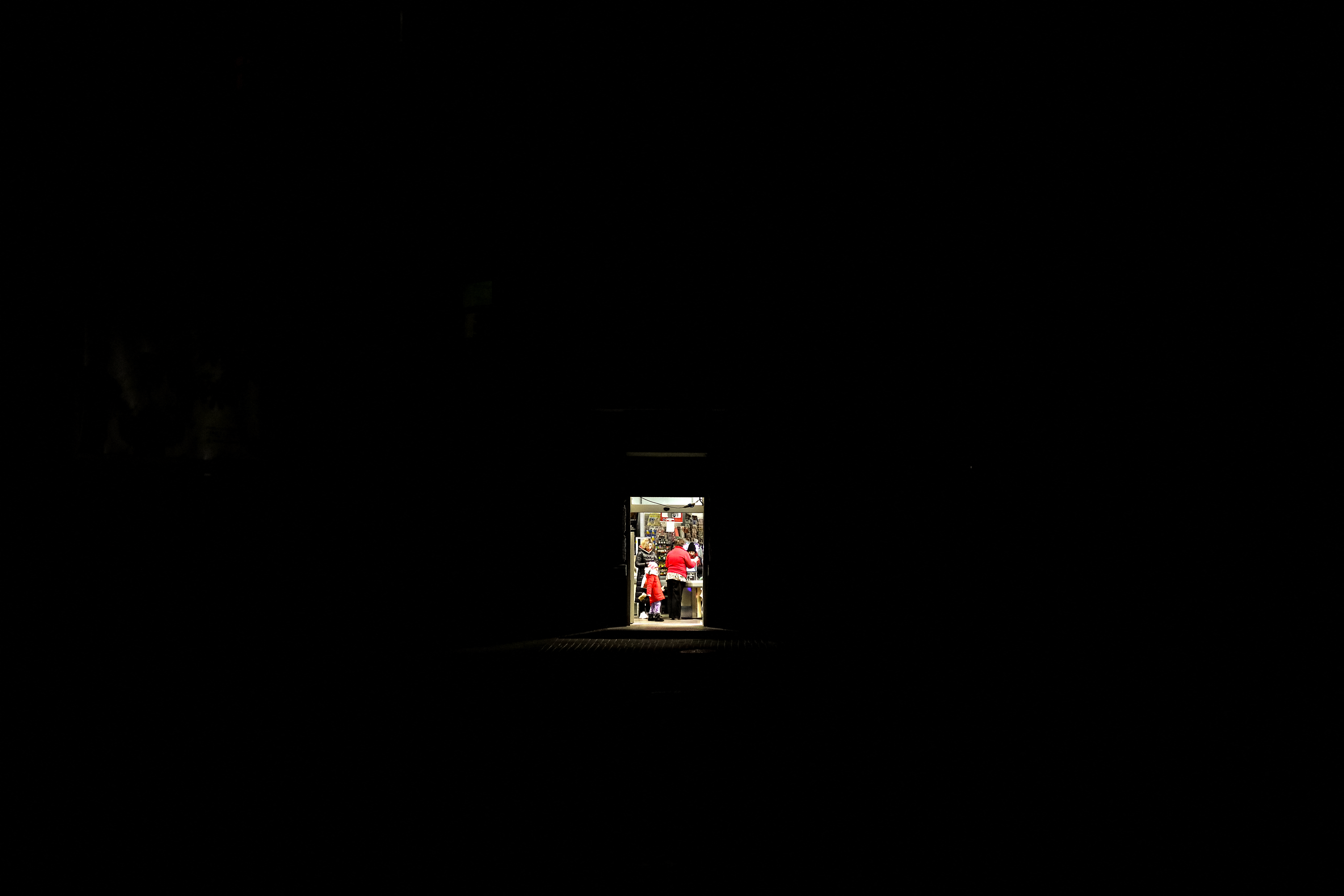 A shop, which still has lighting, stands out in the pitch black of a power cut in Odesa. Some people can be seen in the shop buying goods.