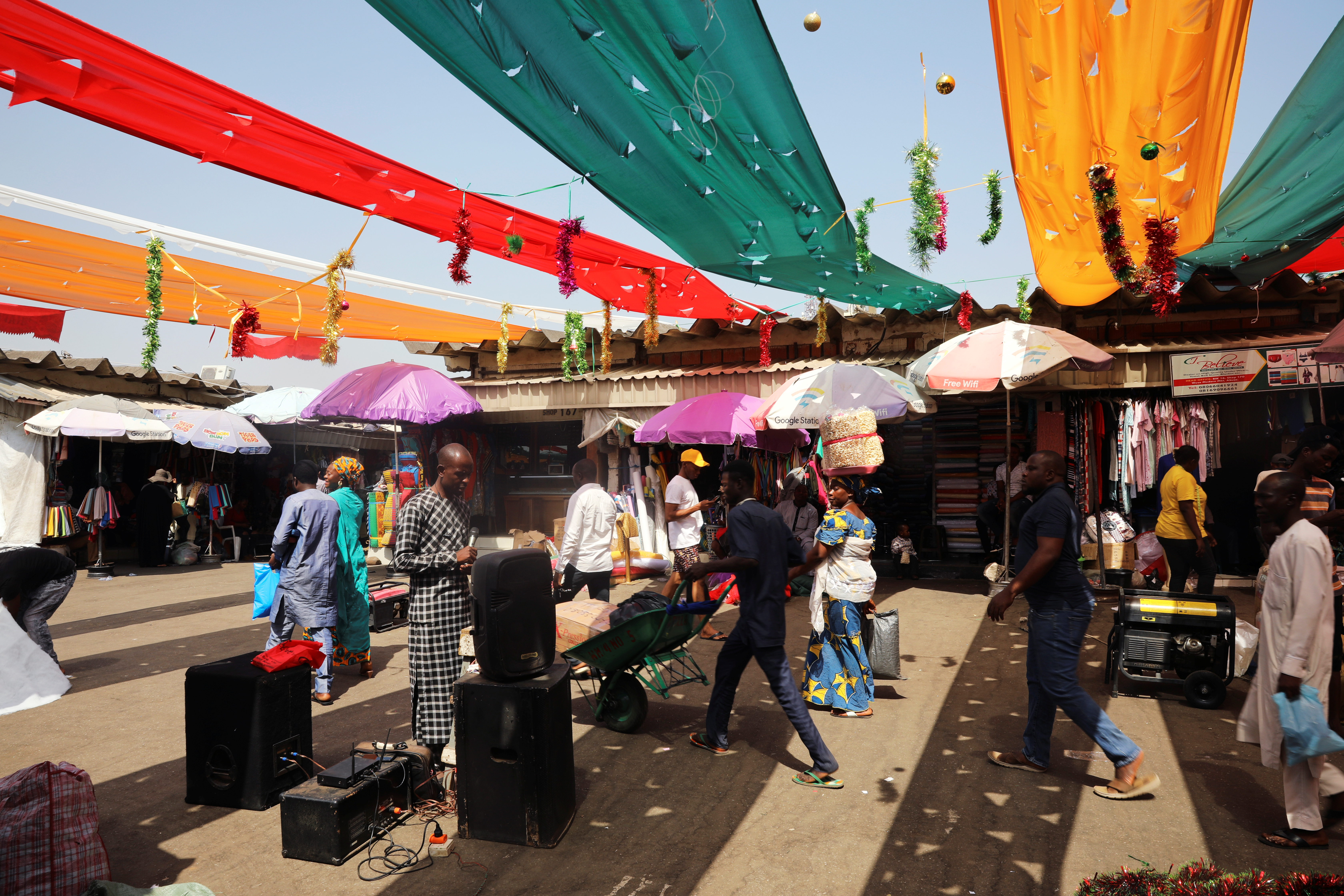 People walk past a street preacher standing at a market, flagged with Christmas decorations in Abuja
