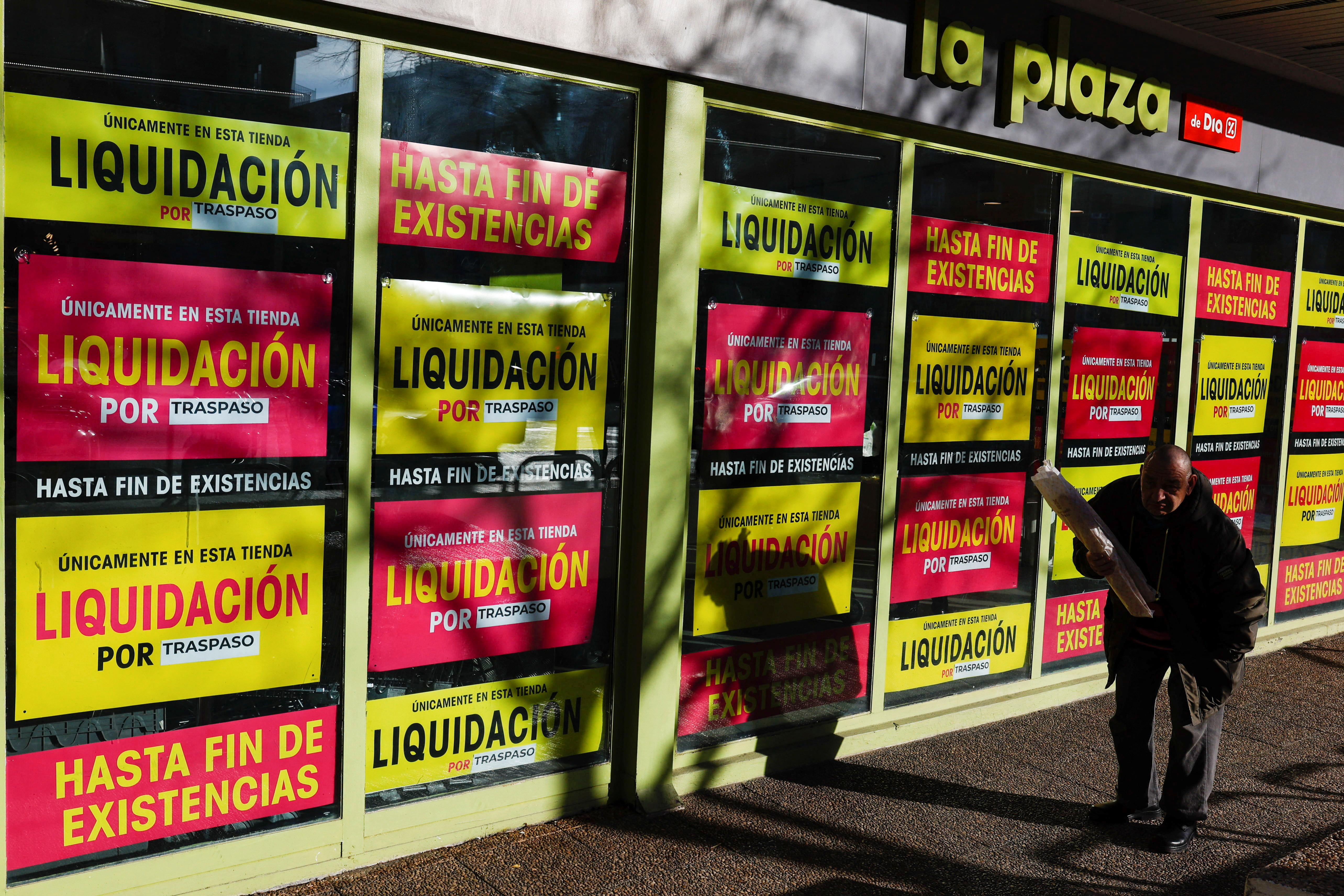 A customer exits a supermarket in Madrid with posters announcing closing down sales