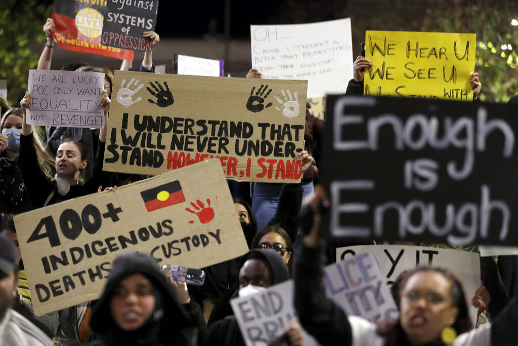 Protestors hold placards that say "Enough is Enough", "400+ Indigenous deaths in custody", "I understand that I will never understand. However, I stand," and "We hear U, We see U"