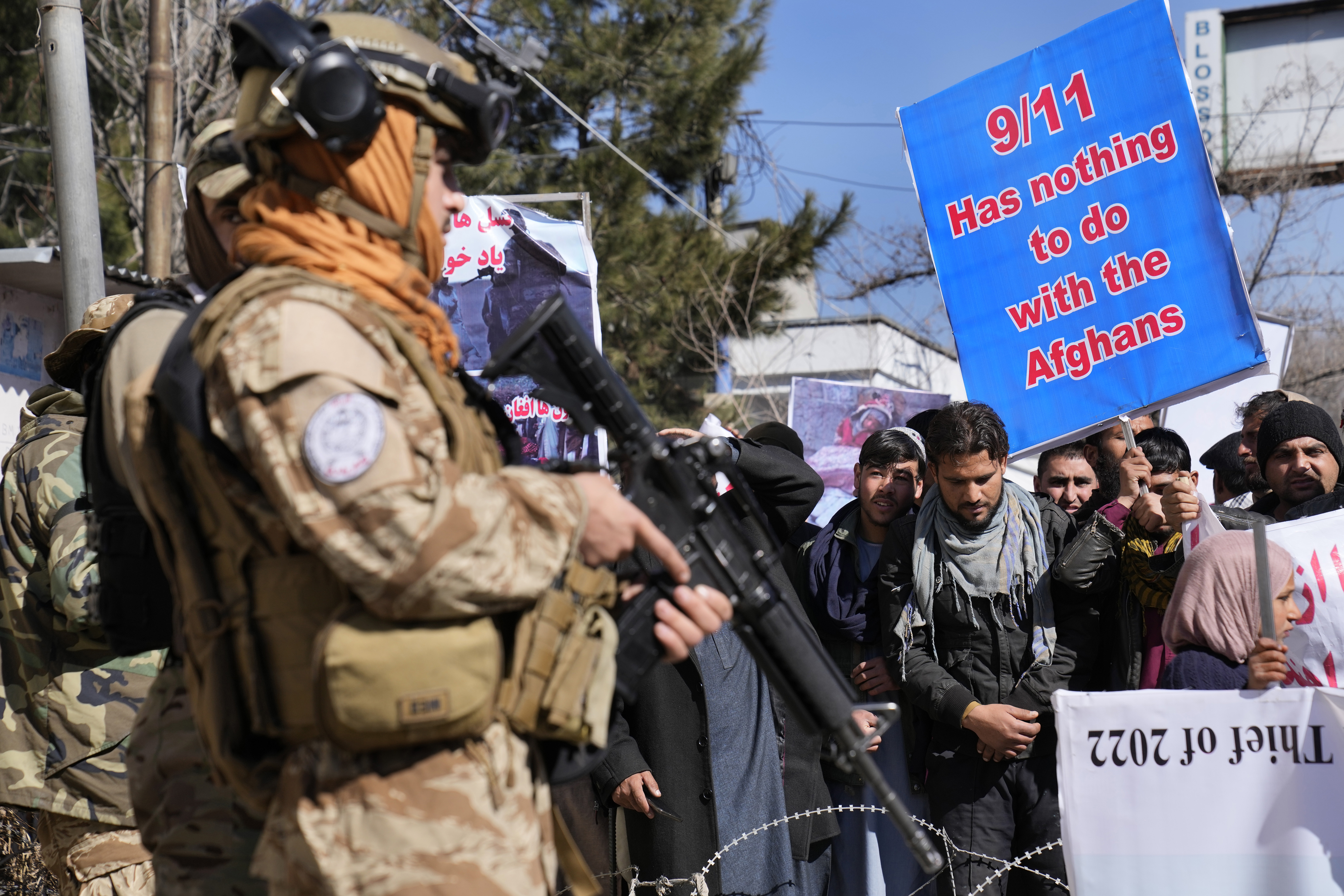 A Taliban fighter stand guards in front of protesters condemning President Joe Biden's decision on frozen Afghan assets in Kabul.