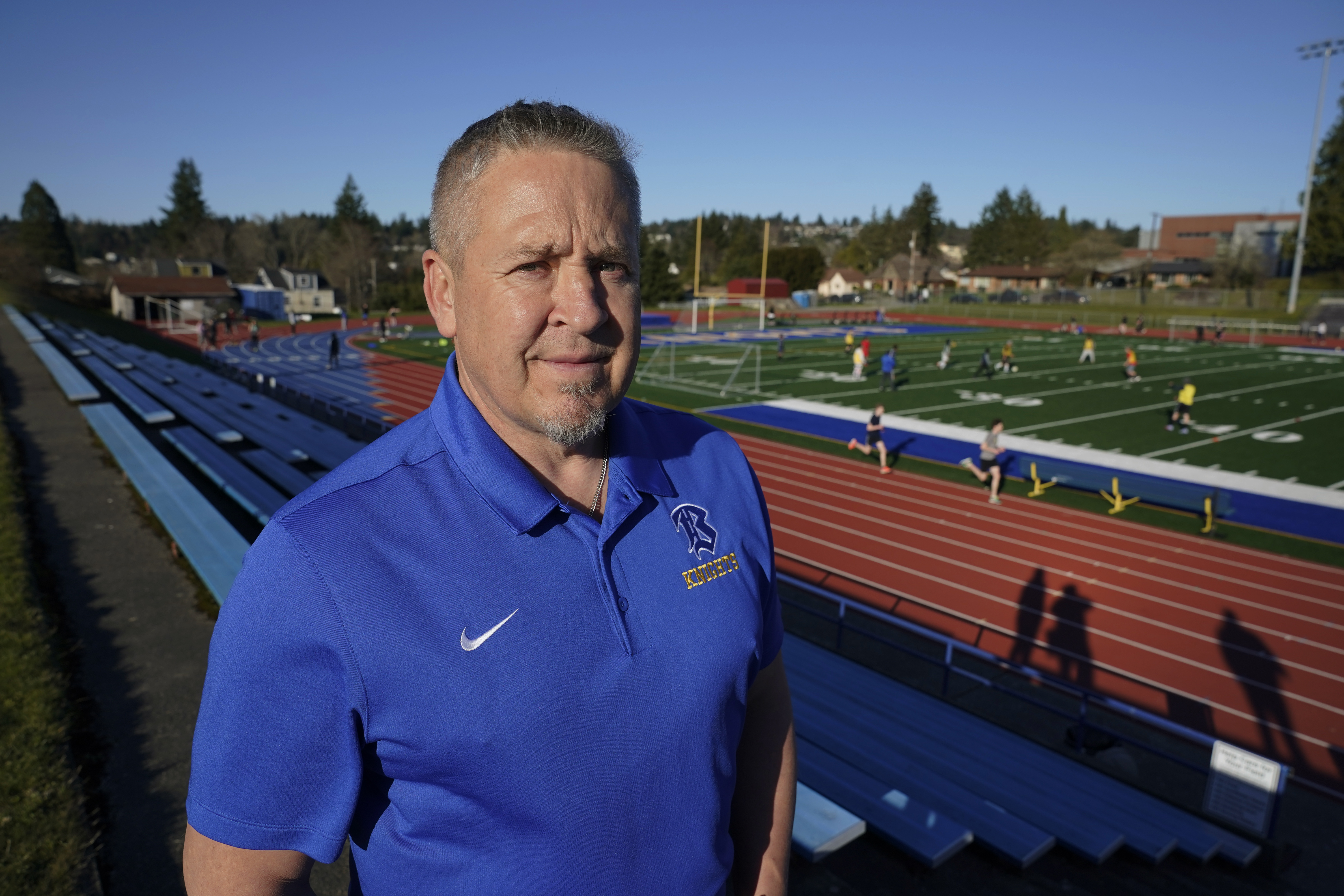 Former coach Joe Kennedy poses in the stands above the field at his former high school workplace
