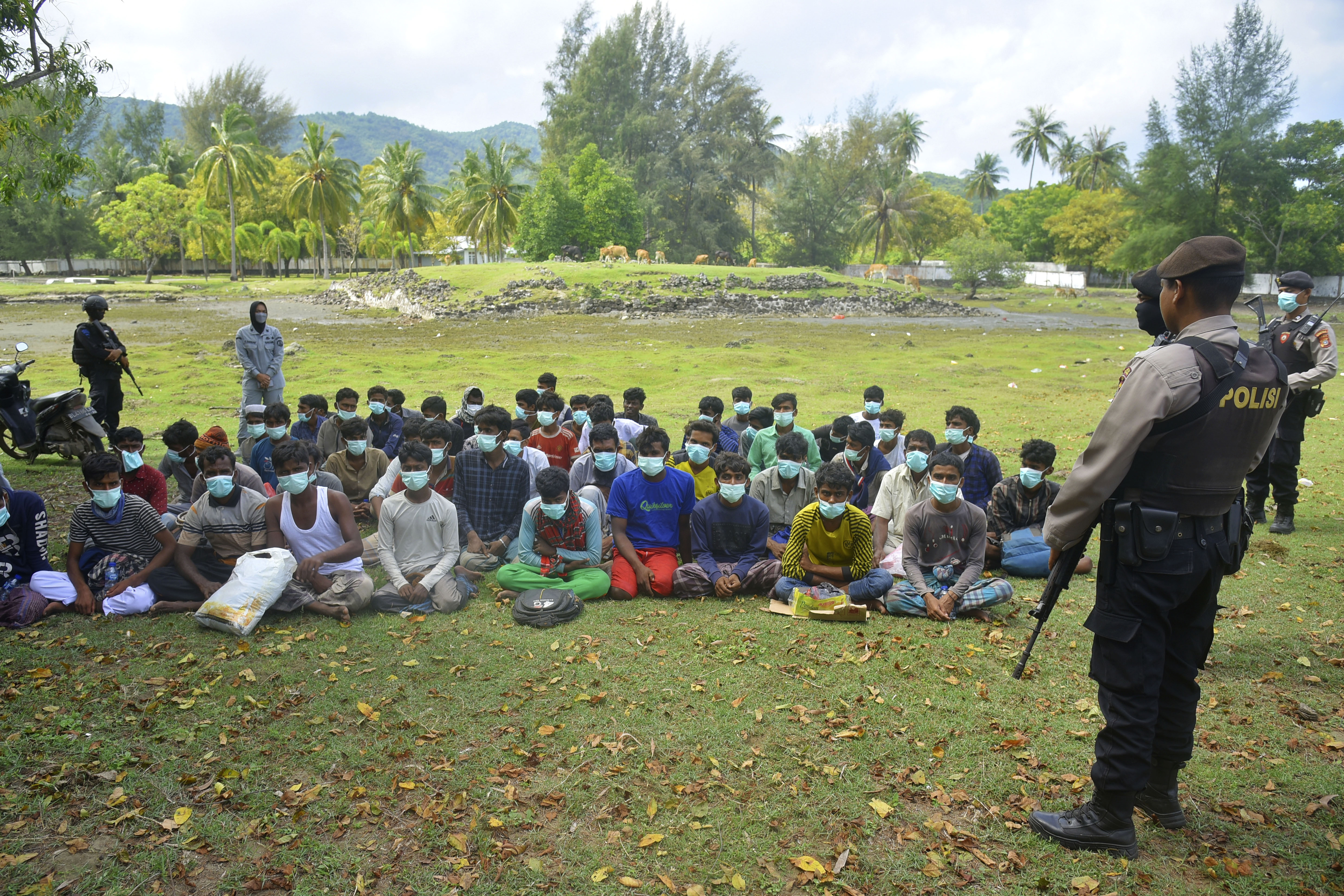 Indonesian police officers watch a group of ethnic Rohingya people after they landed on Indra Patra beach