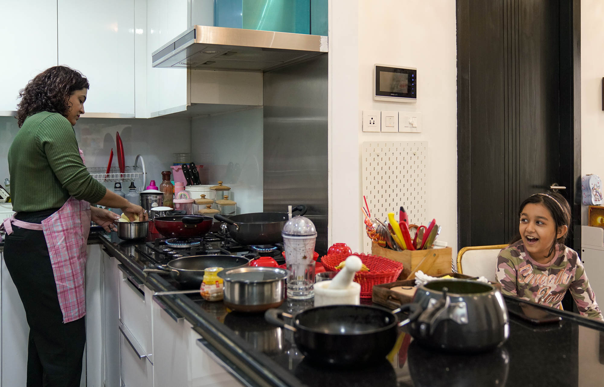 Khushboo is in the kitchen, preparing food, while her daughter sits at the other side of the counter talking to her