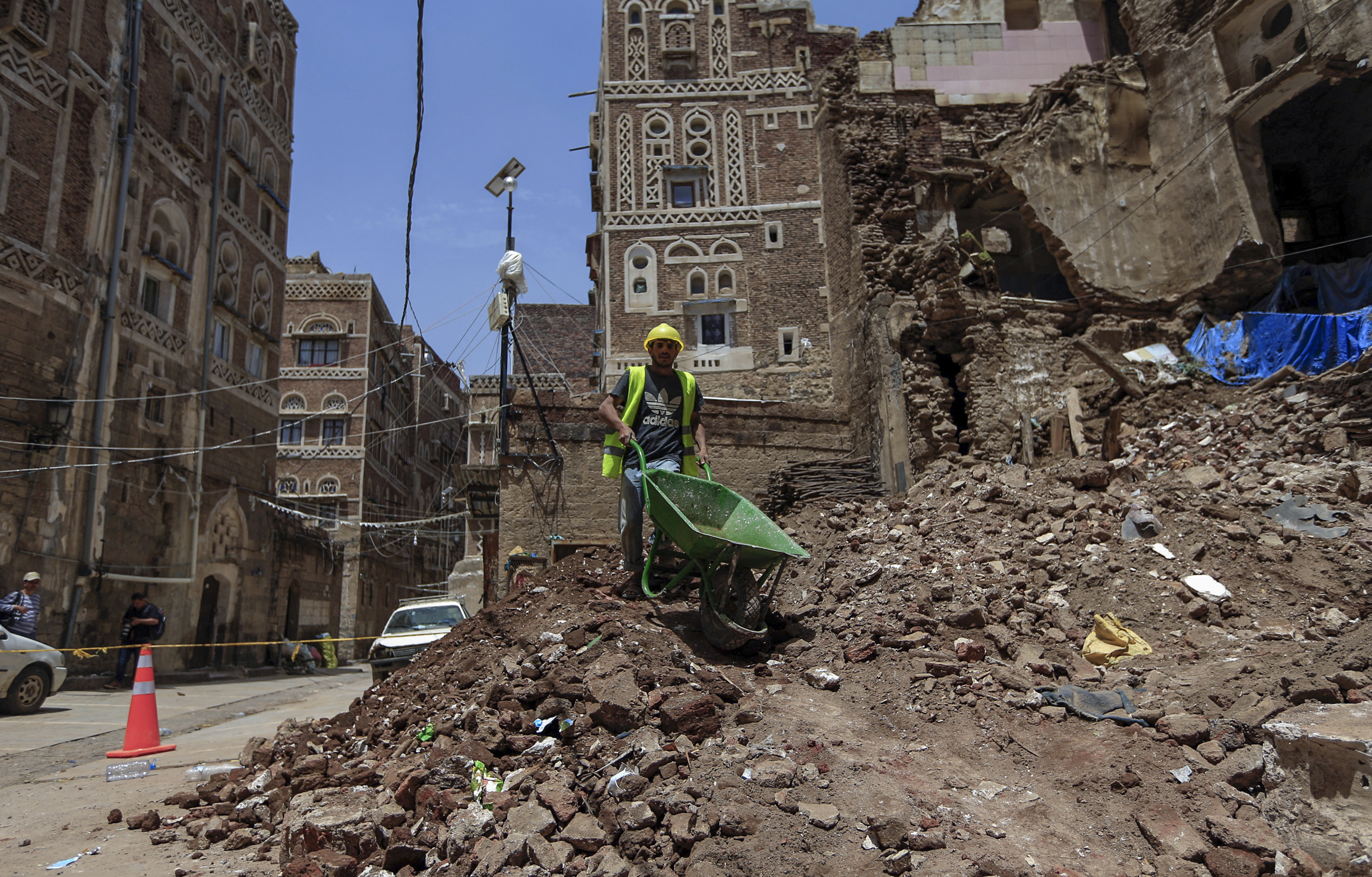 A photo of a man holding a wheelbarrow and standing in rubble.