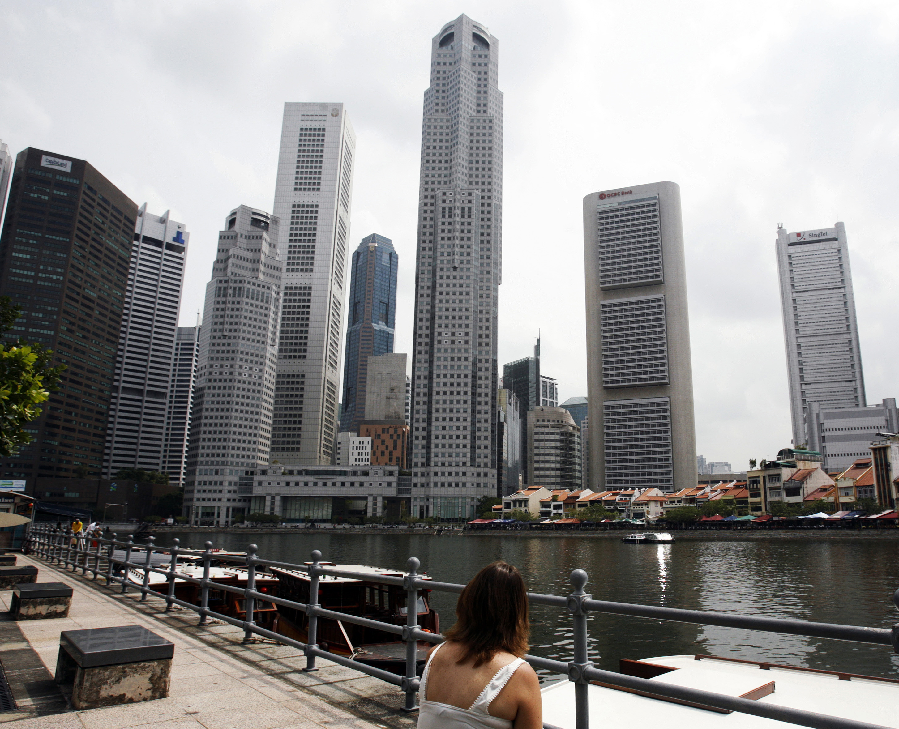 A woman sits looking at the skyline of Singapore's financial district.