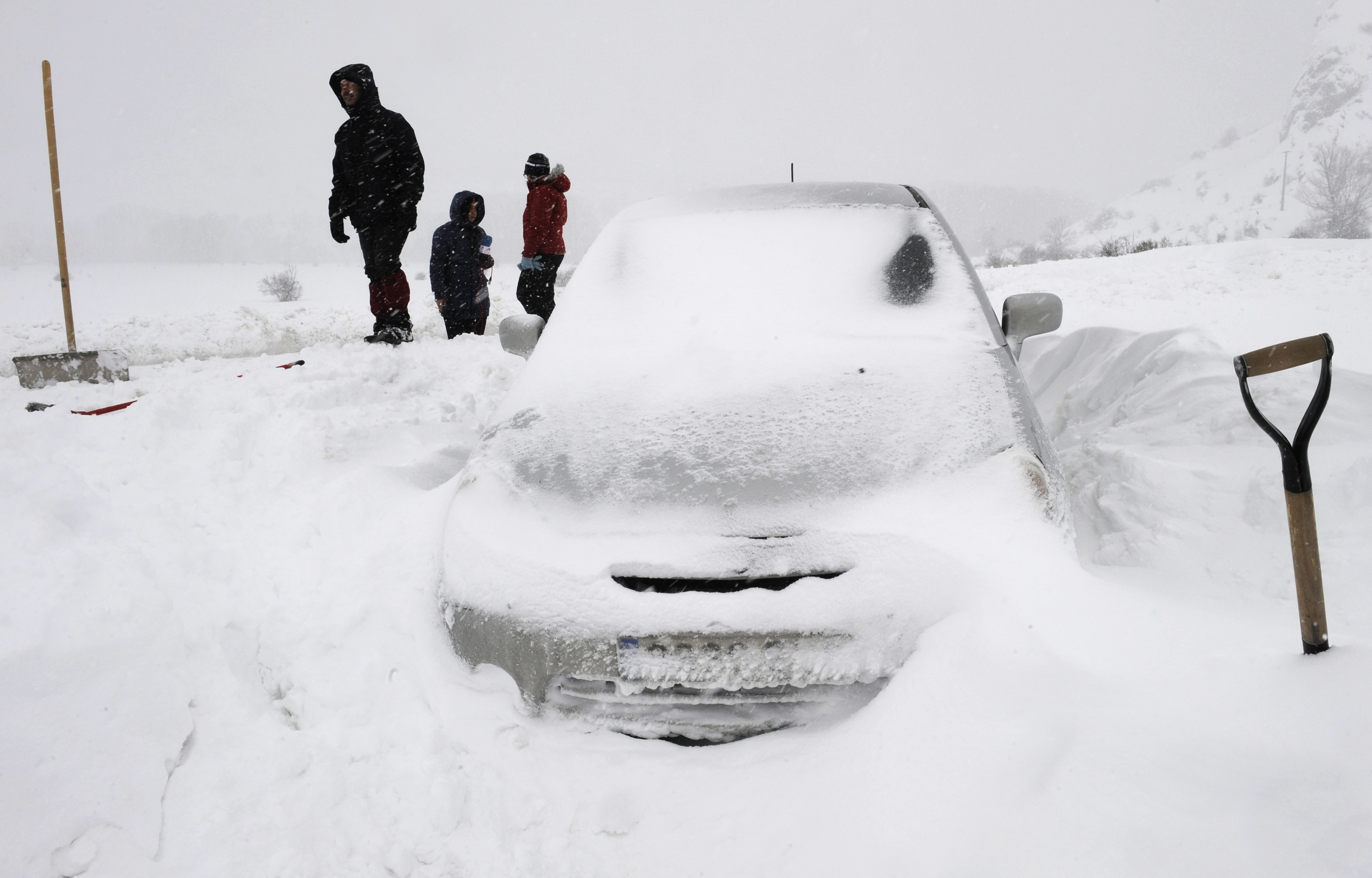 People stand near a car which got stranded during a snowstorm near Barrios de Luna, in northern Spain, February 5, 2015. REUTERS/Eloy Alonso (SPAIN - Tags: ENVIRONMENT SOCIETY)