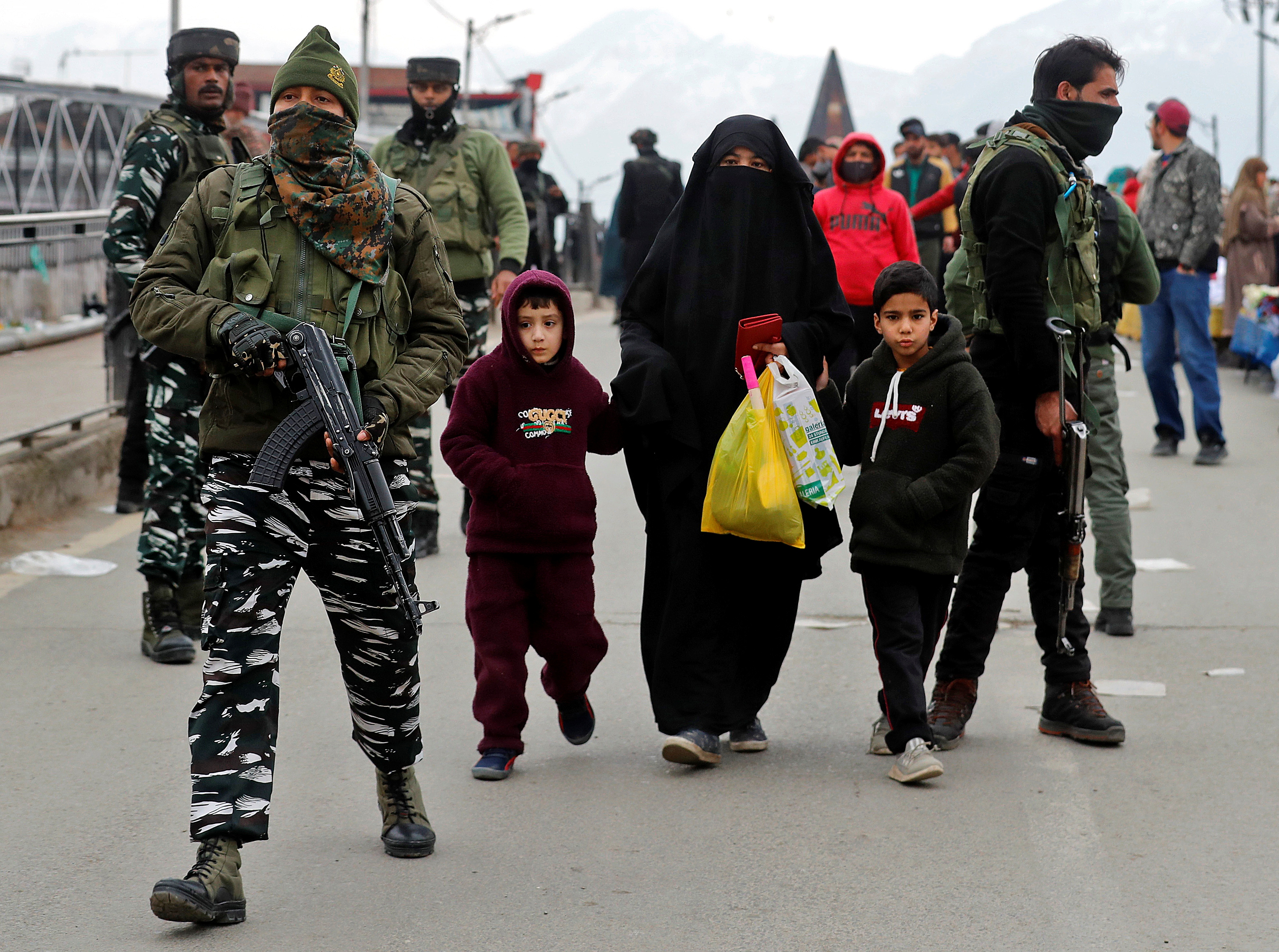 A veiled woman walks with her children past Indian security force personnel near the site of a grenade explosion in Srinagar in Indian-administered Kashmir.
