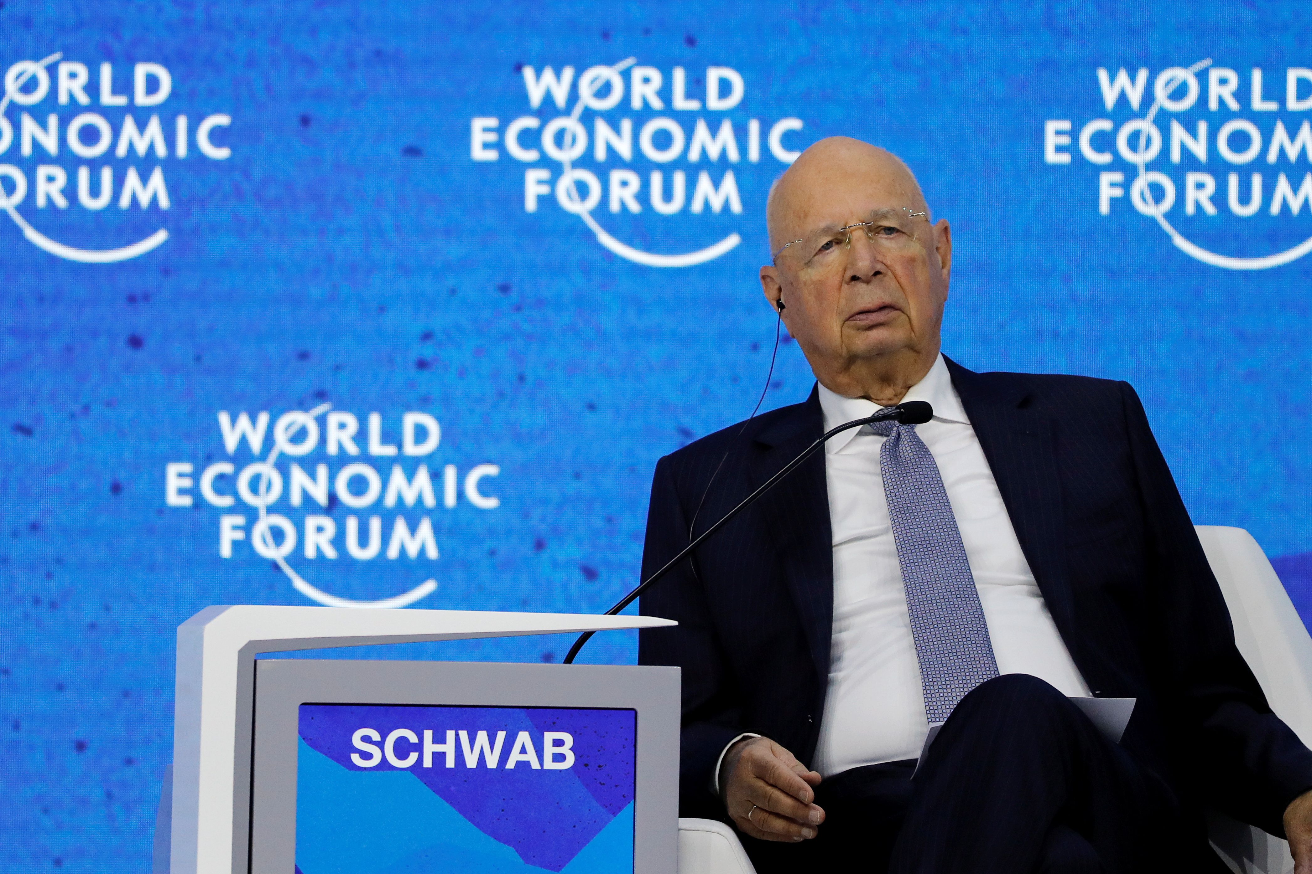 Klaus Schwab sits on a chair at the World Economic Forum listening to a speaker