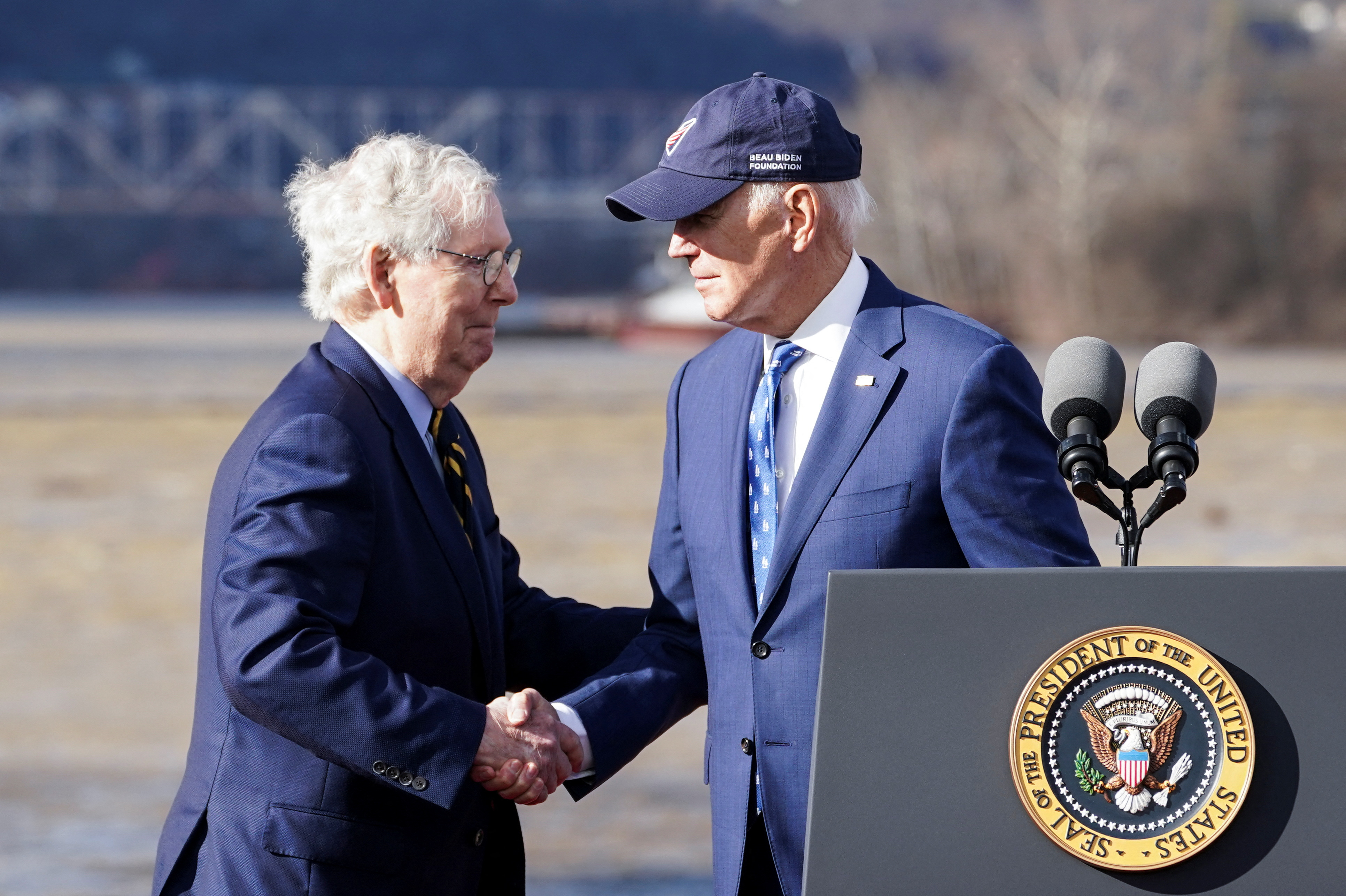 Joe Biden and Mitch McConnell shake hands in front of the Brent Spence Bridge