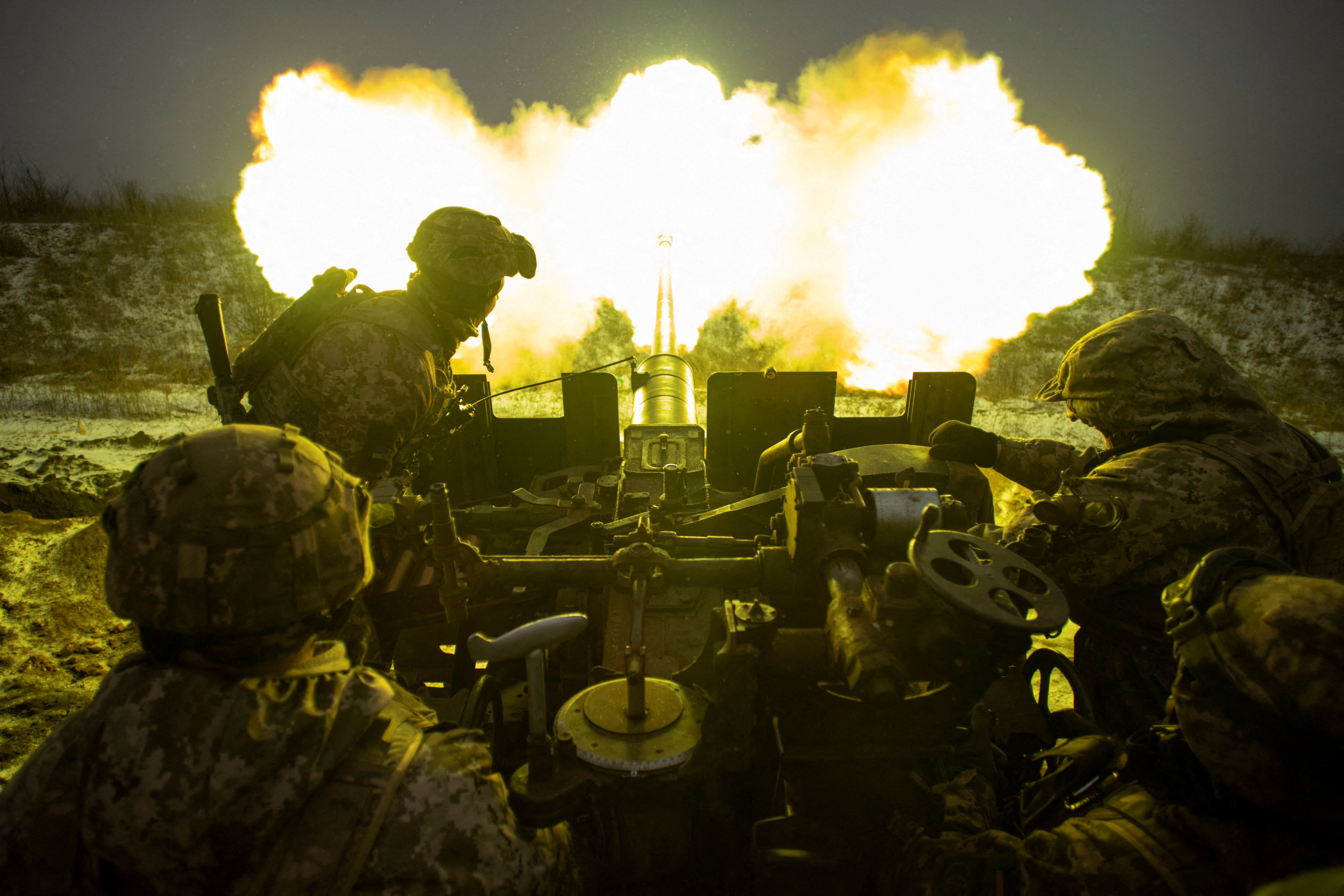 Ukrainian service members fire an anti-aircraft gun towards Russian positions on a frontline near the town of Bakhmut, Ukraine. The nozzle of the gun in engulfed in flames that lights up the silhouetted troops.