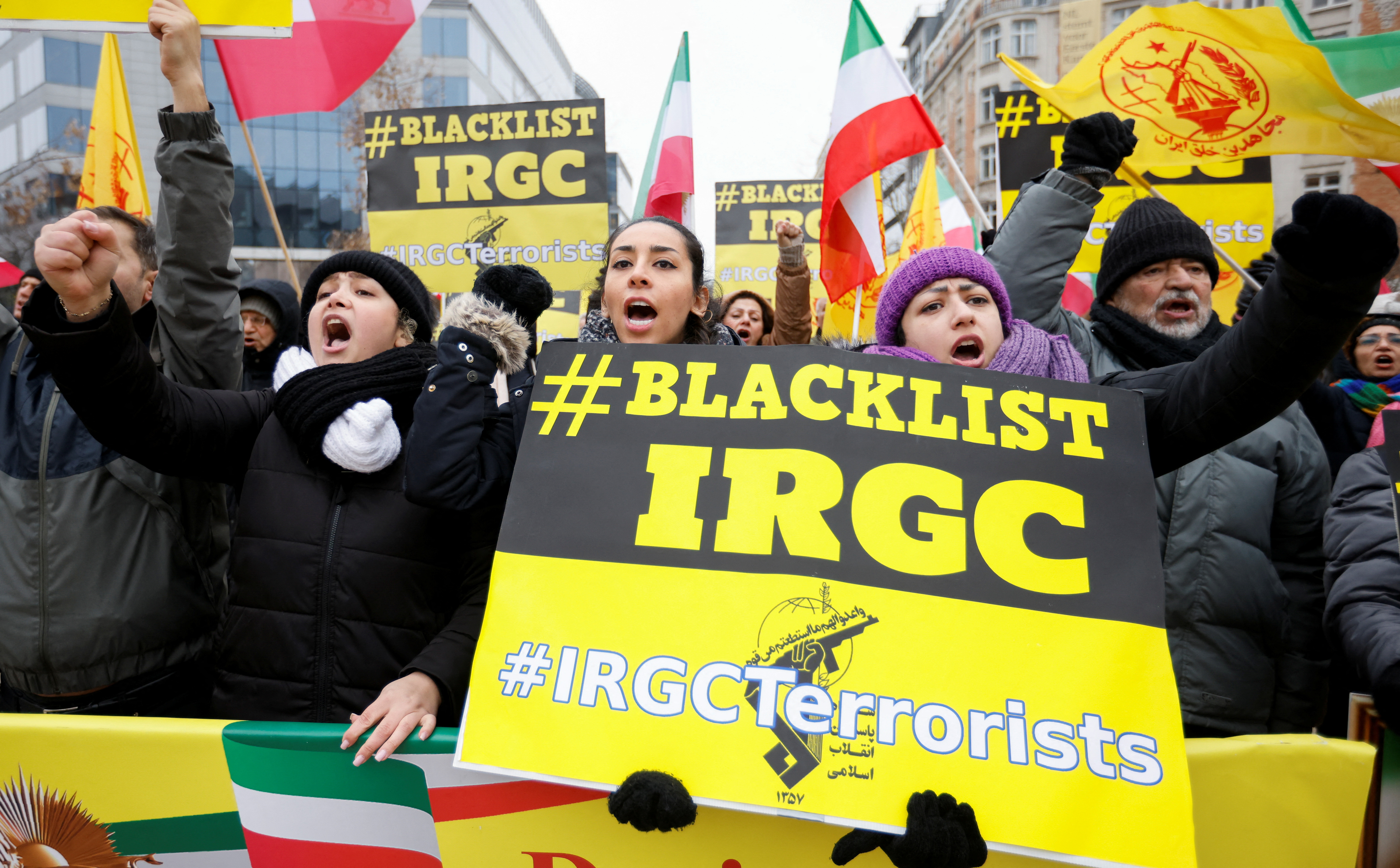 Protesters wave flags and hold placards, one of which says 'Blacklist IRGC'