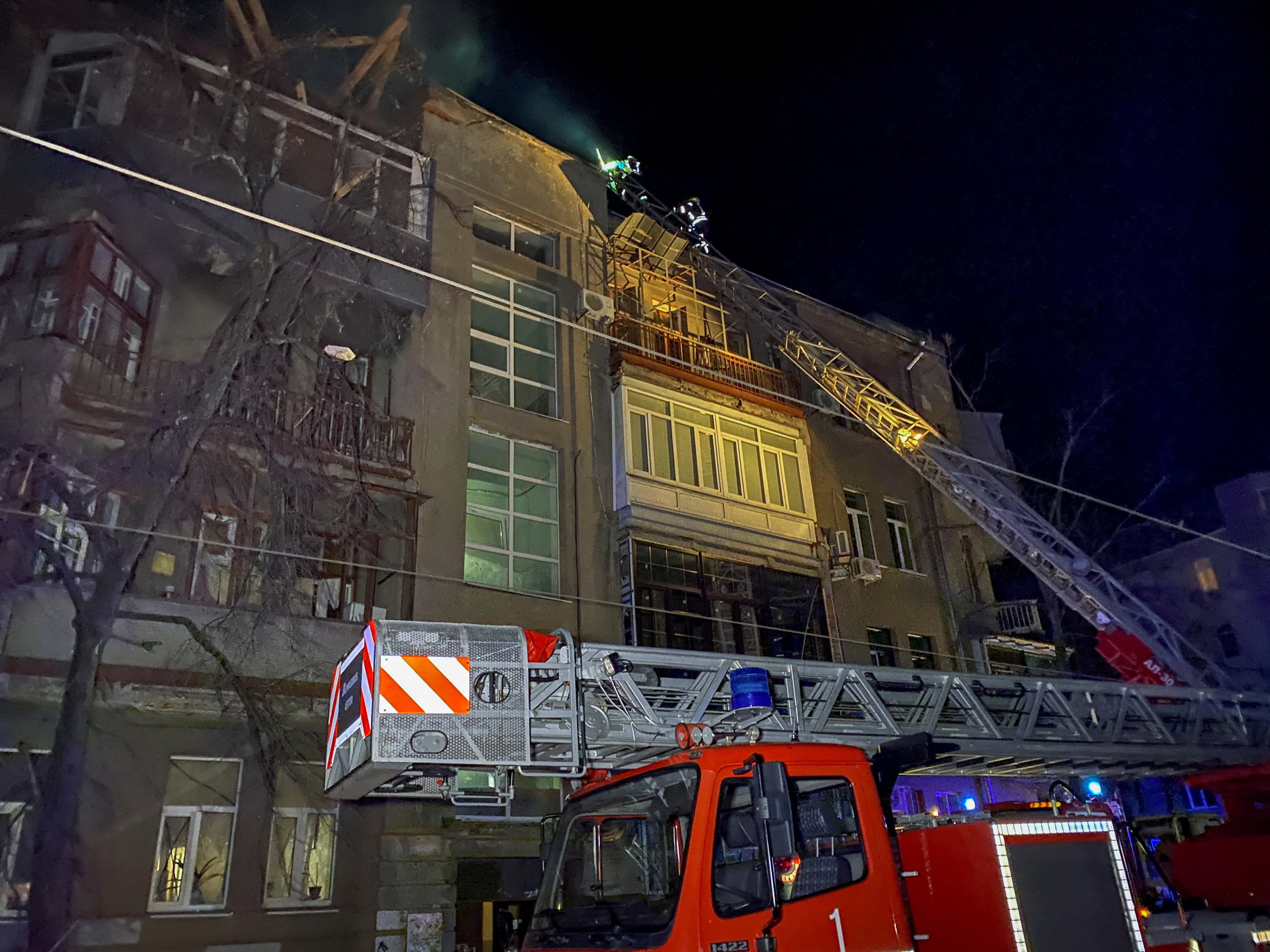 A fire engine at the side of a bombed building in Kharkiv, Ukraine. It's dark, but there is damage to the top of the building.