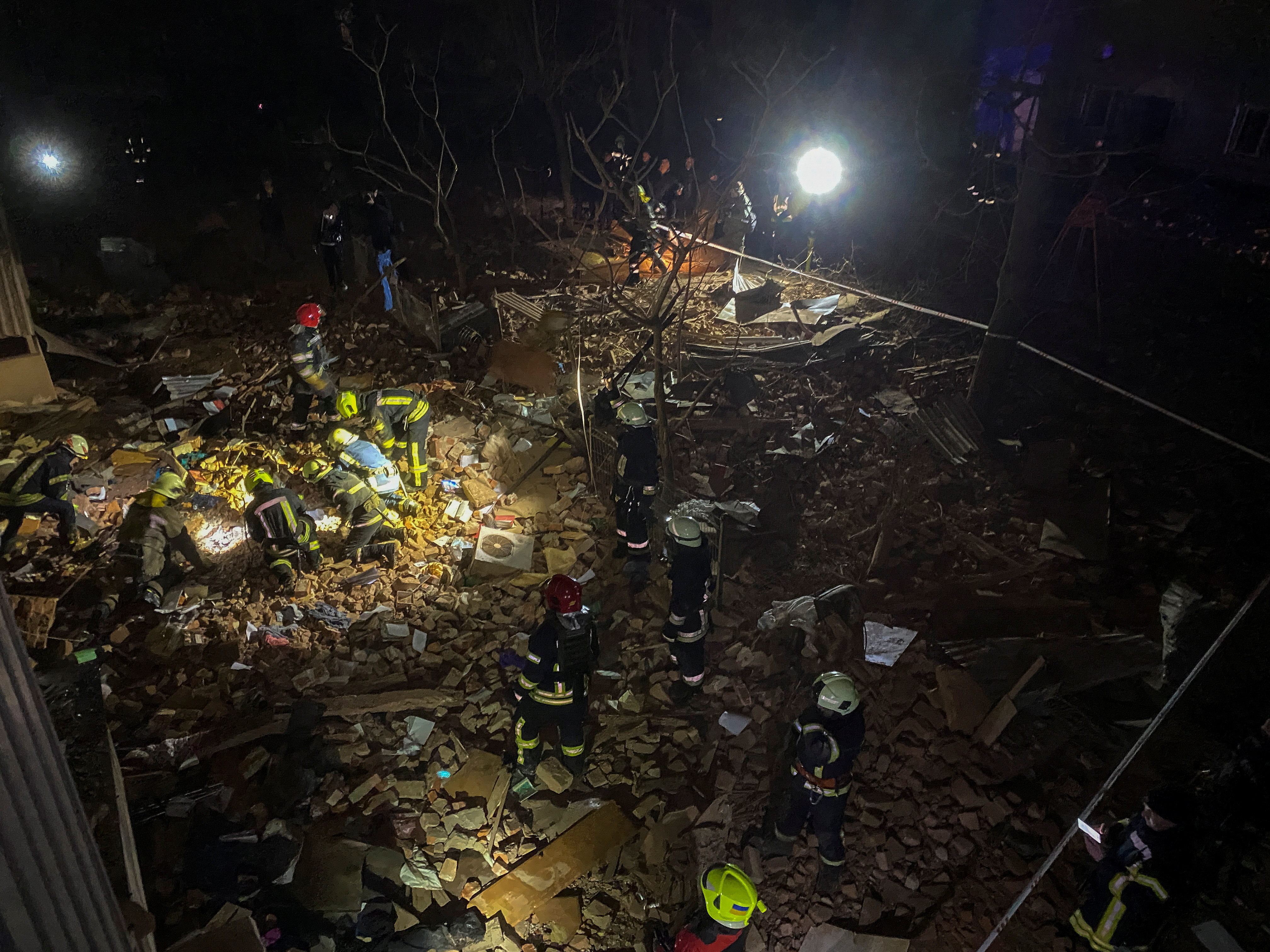 Rescue workers amid the rubble of the ruined Kharkiv apartment block. It is illuminated by a flood light